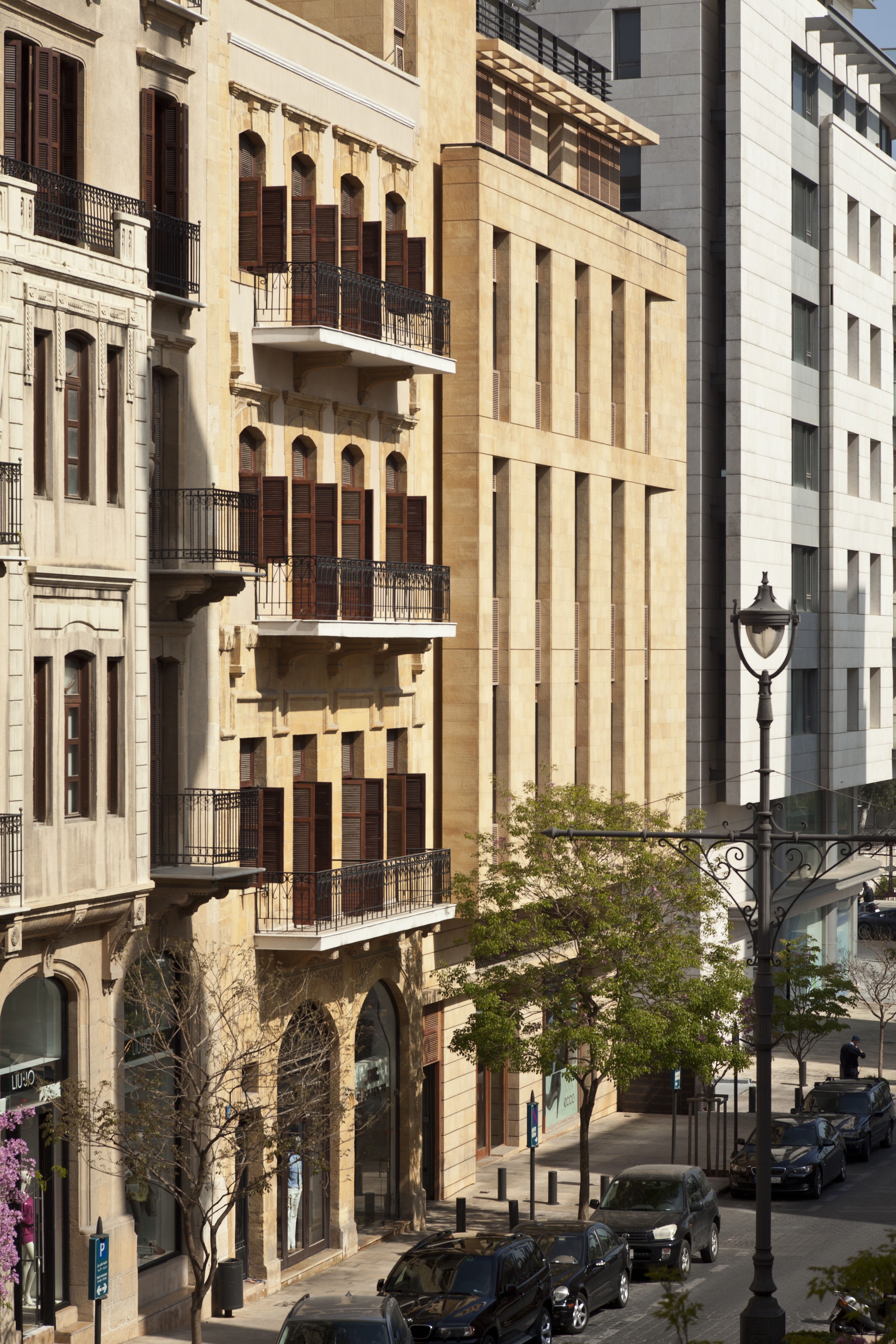 Waqf Foch Office Building in Beirut, its stone facade with vertical fins standing beside restored heritage buildings with wooden shutters on a tree-lined street