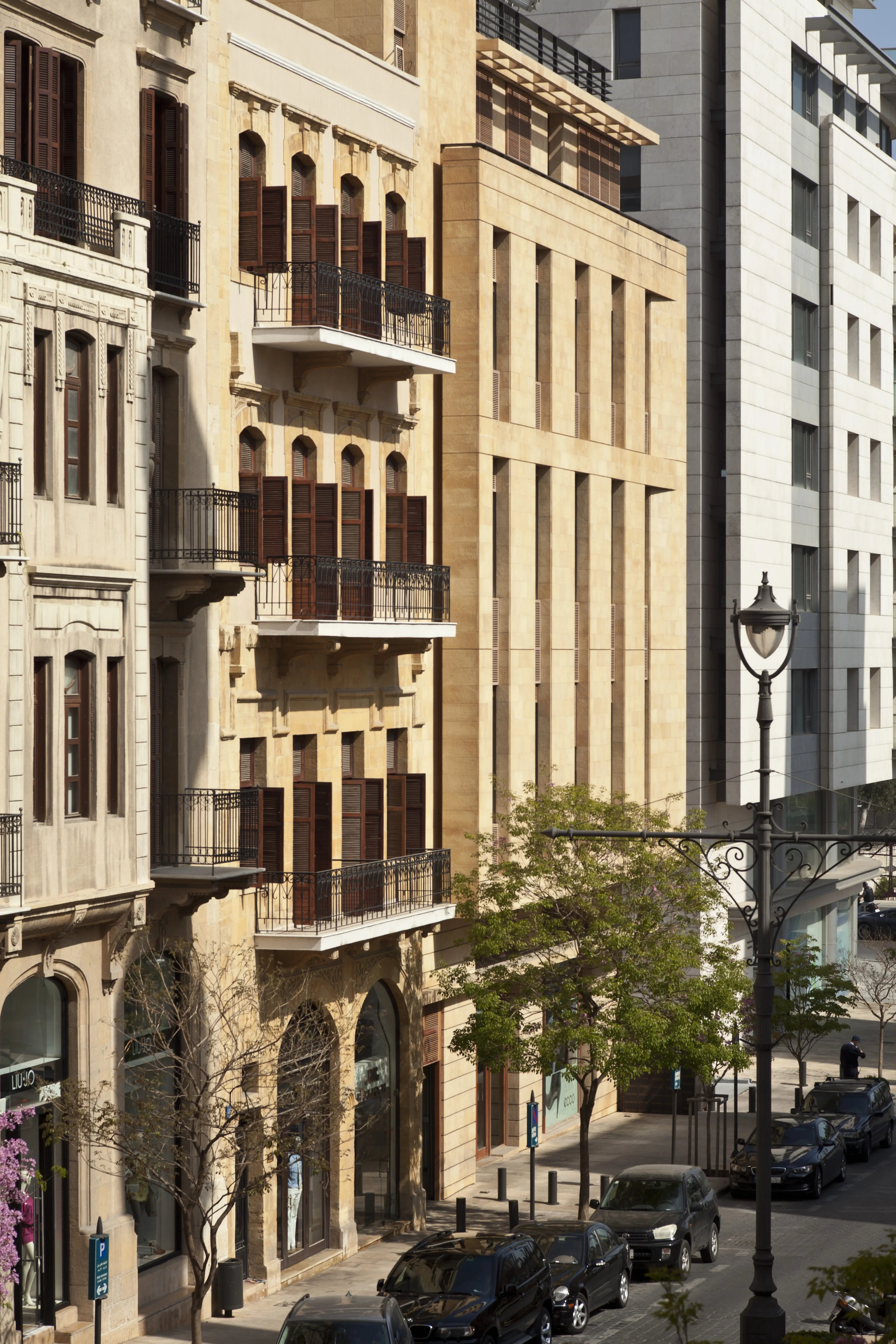 Waqf Foch Office Building in Beirut, its stone facade with vertical fins standing beside restored heritage buildings with wooden shutters on a tree-lined street