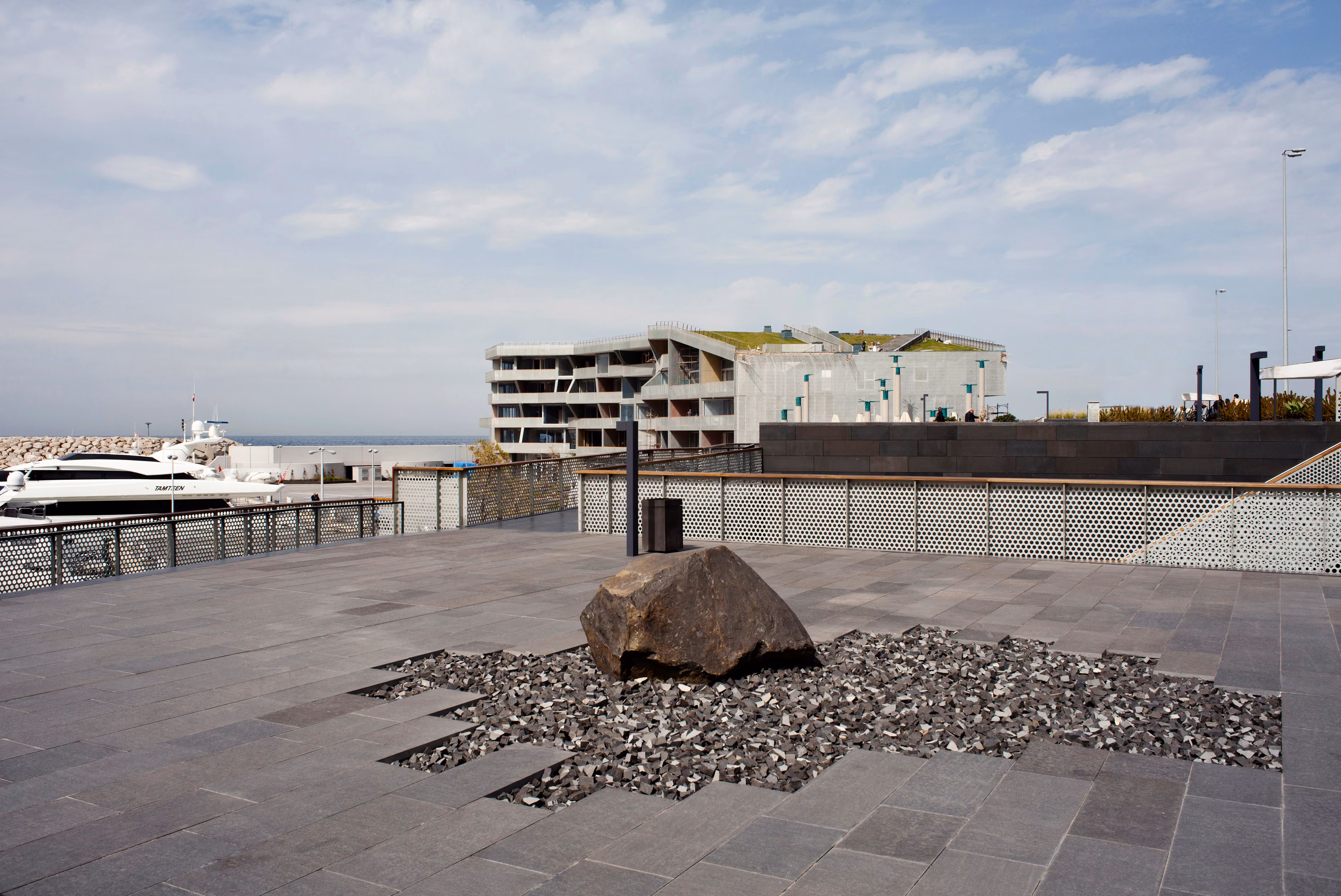 Paved quayside plaza at Beirut Marina & Town Quay with a large boulder set in dark gravel, moored yachts and the terraced apartment building beyond