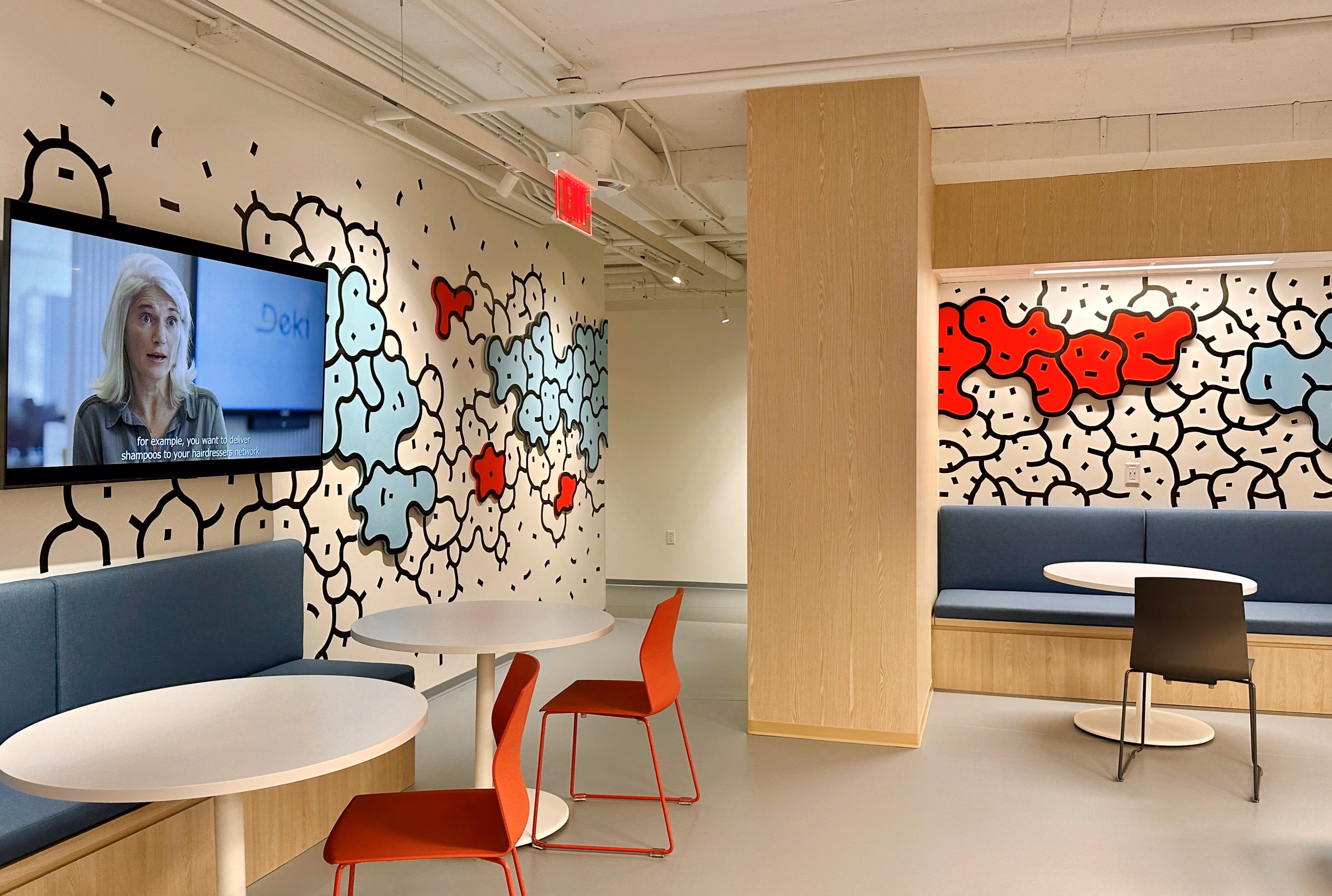 Lounge area in Zebox Washington with playful cloud-shaped wall graphics, round tables, red chairs and blue banquette seating beneath a wall-mounted screen