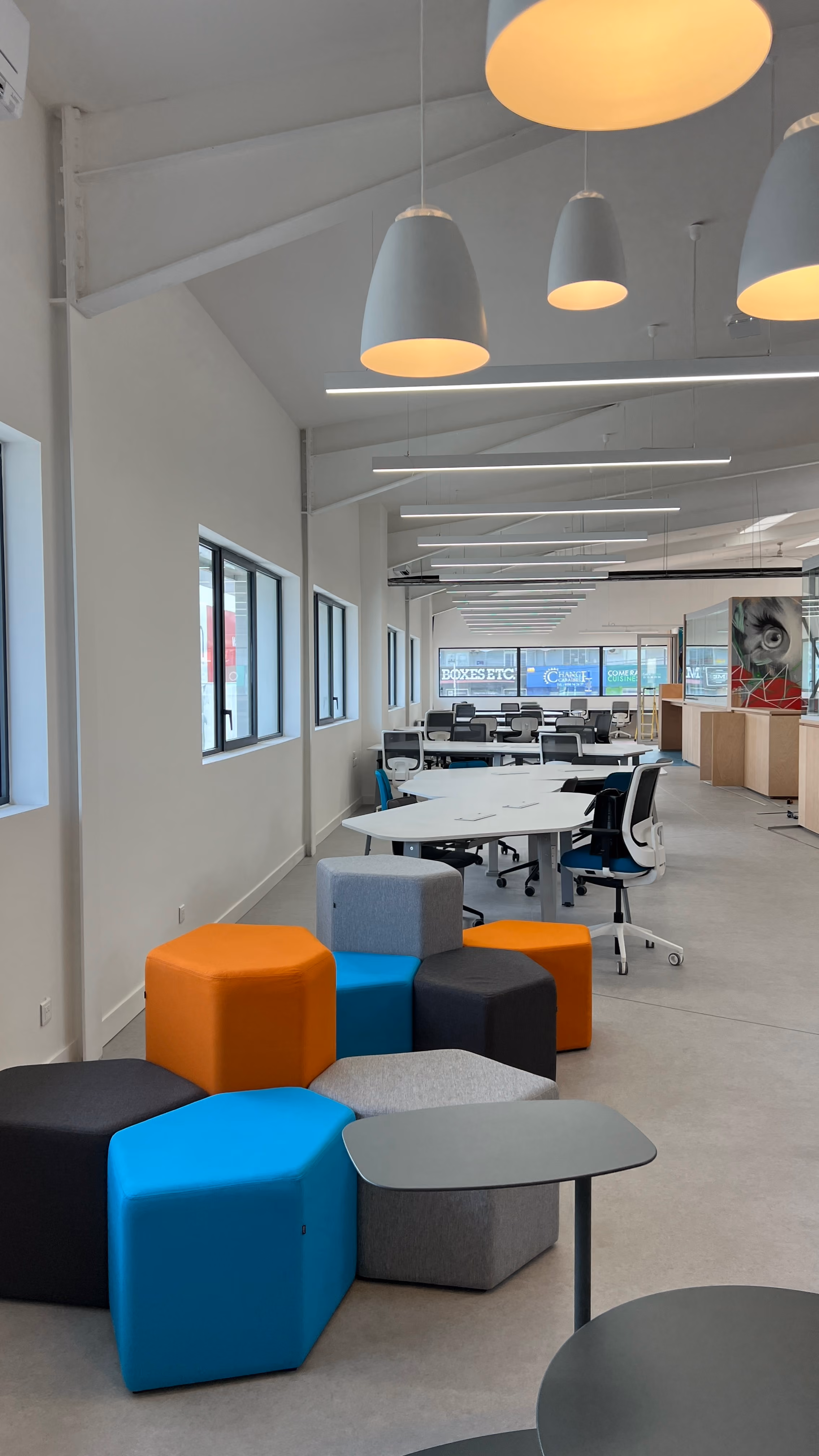 Colourful hexagonal poufs and shared work tables in Zebox Guadeloupe's open office, with pendant lighting under an exposed sloped ceiling