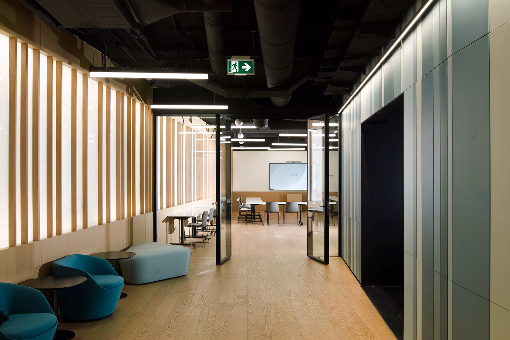 Lounge corridor at Lot 114 in Beirut, wood-slat walls and teal armchairs leading to an open meeting room with a screen and movable tables