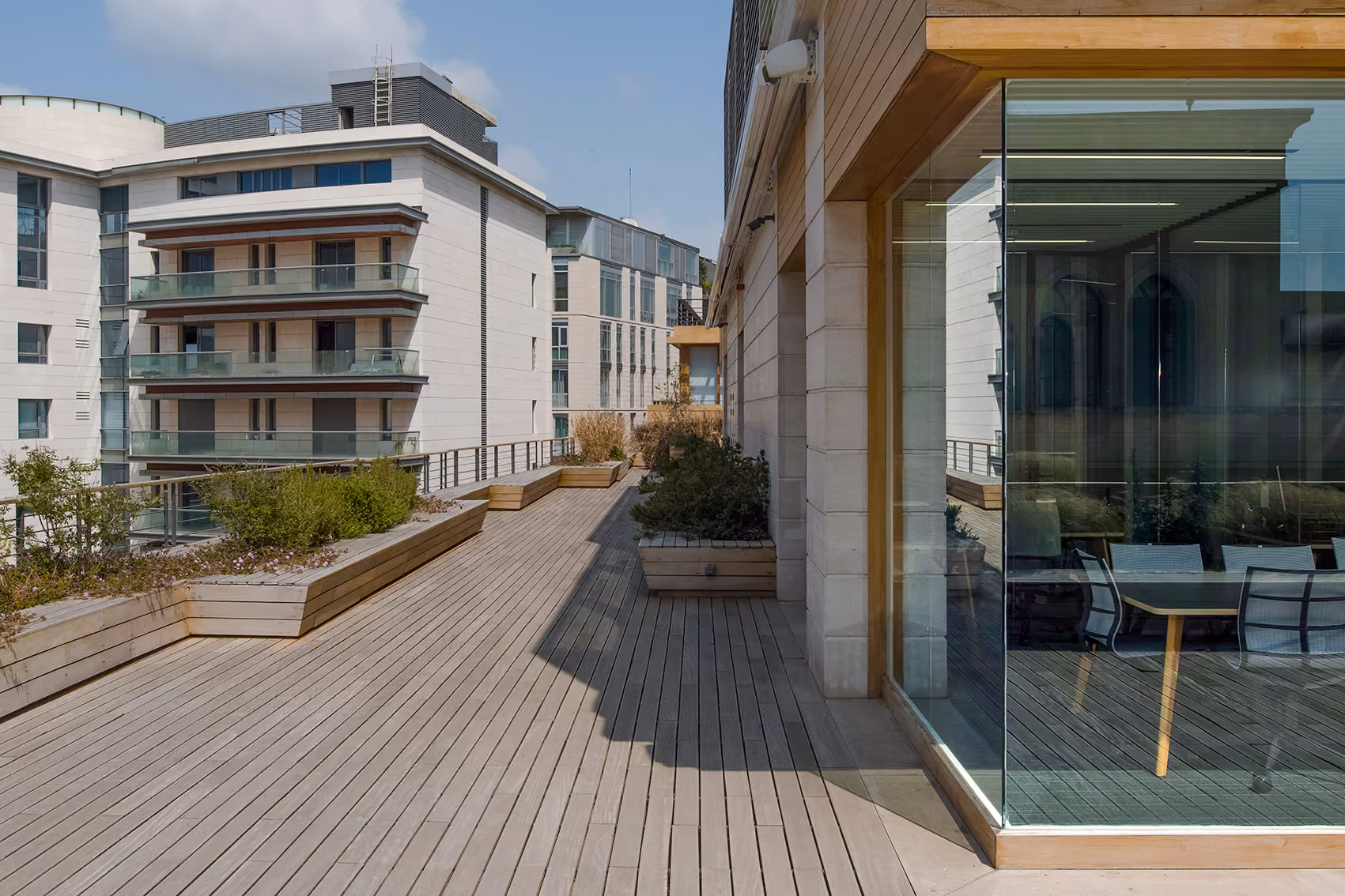 Wooden-decked rooftop terrace at Lot 114 in Beirut, with planters, glazed meeting room and surrounding stone-clad apartment buildings