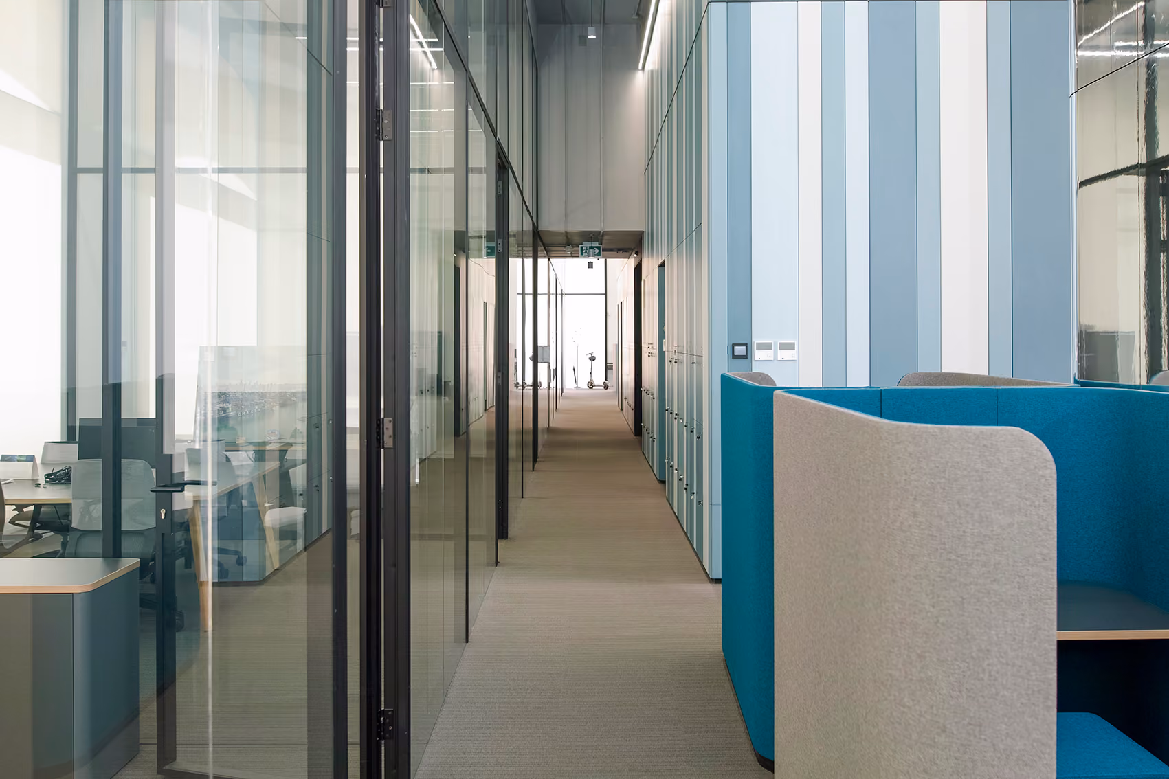 Interior corridor at Lot 114 in Beirut, glass-walled offices beside striped blue cabinetry and a teal upholstered booth