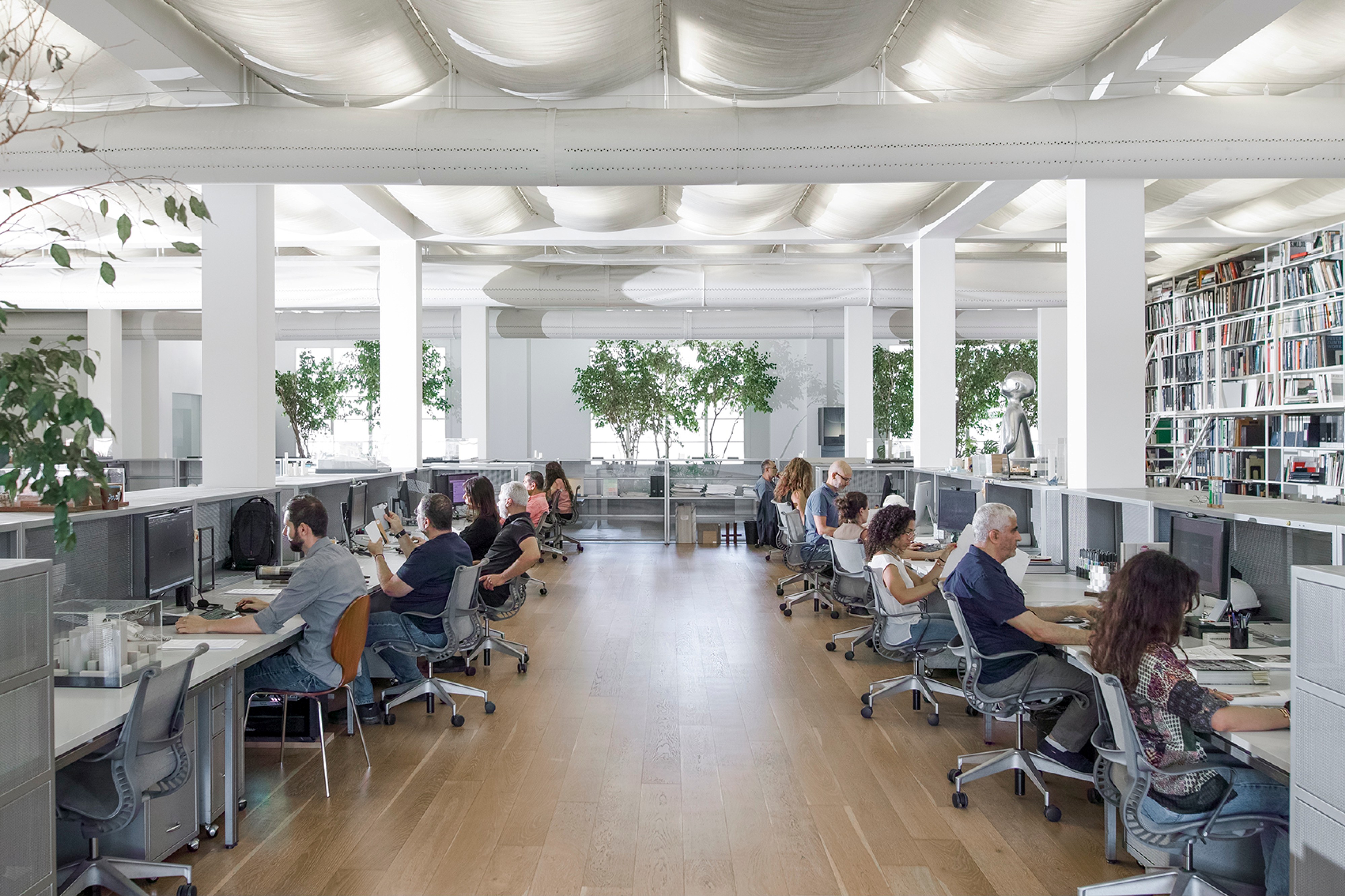 ngª Office in Beirut by Nabil Gholam Architects, an open-plan workspace with wooden flooring, staff at long desks, indoor plants and a draped fabric ceiling