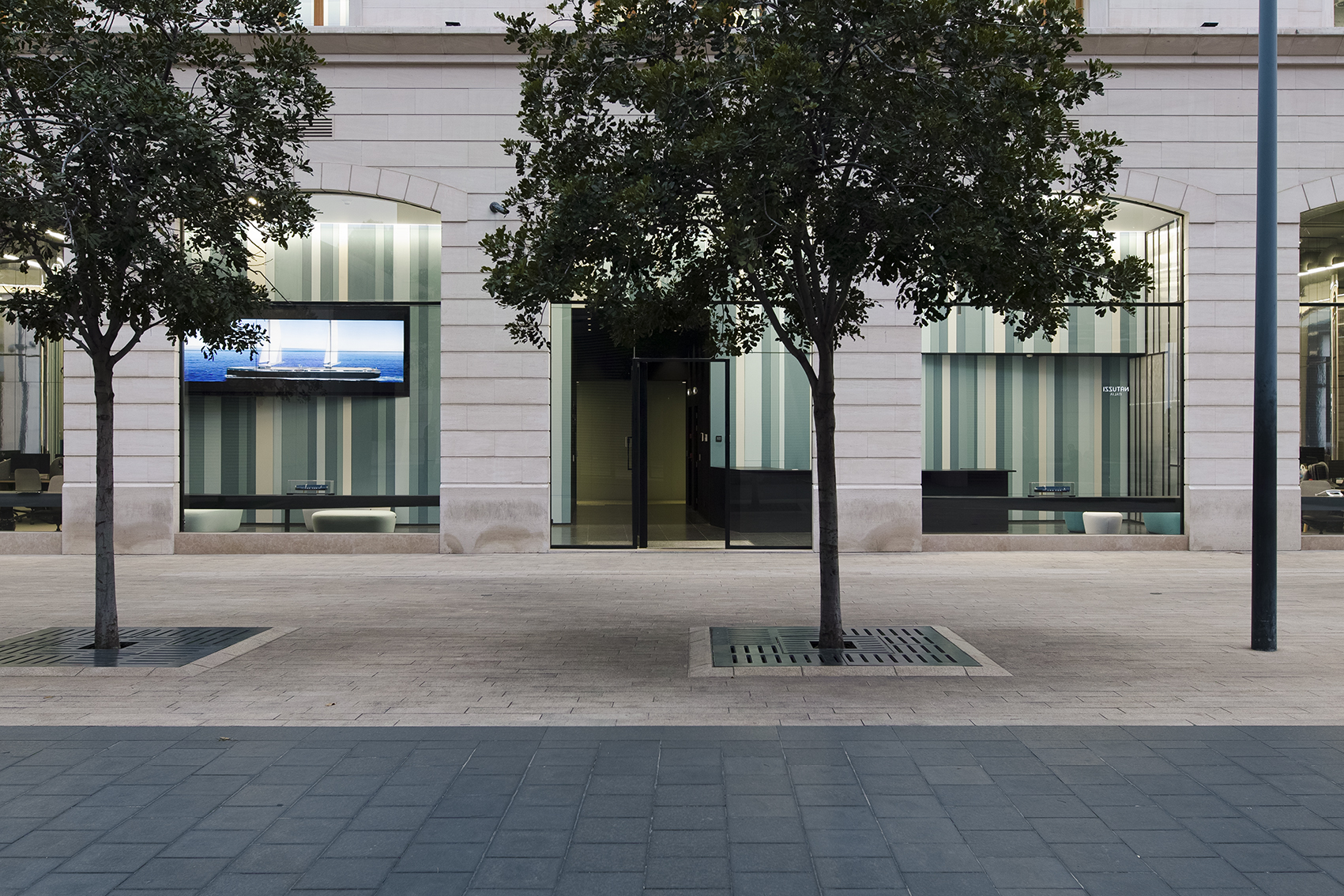 Ground floor storefronts of Lot 114 in Beirut, striped glass facades framed by trees along a paved pedestrian plaza