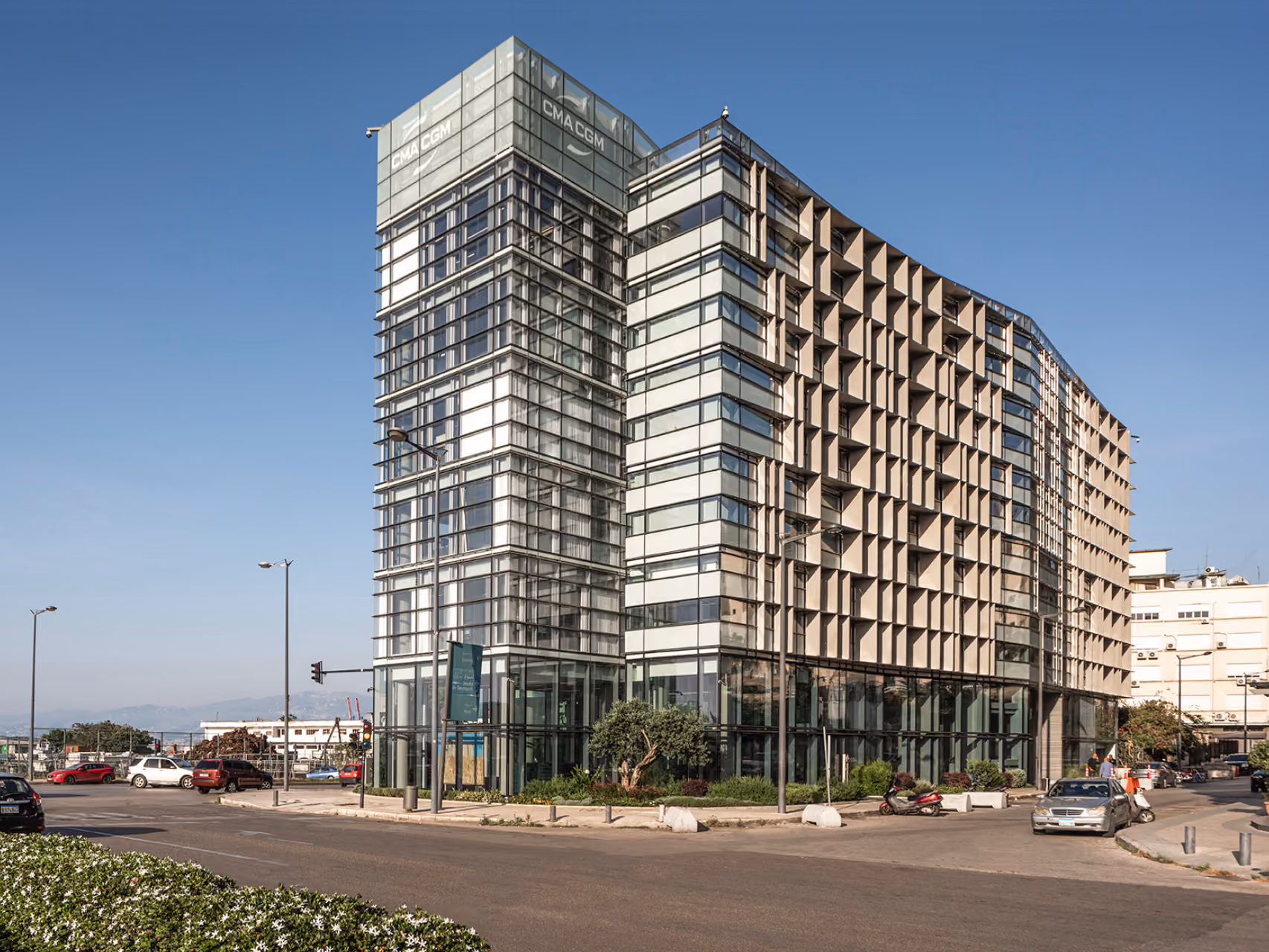 Street-level view of the refurbished CMA-CGM Headquarters in Beirut, showing its glazed corner tower and perforated concrete brise-soleil facade