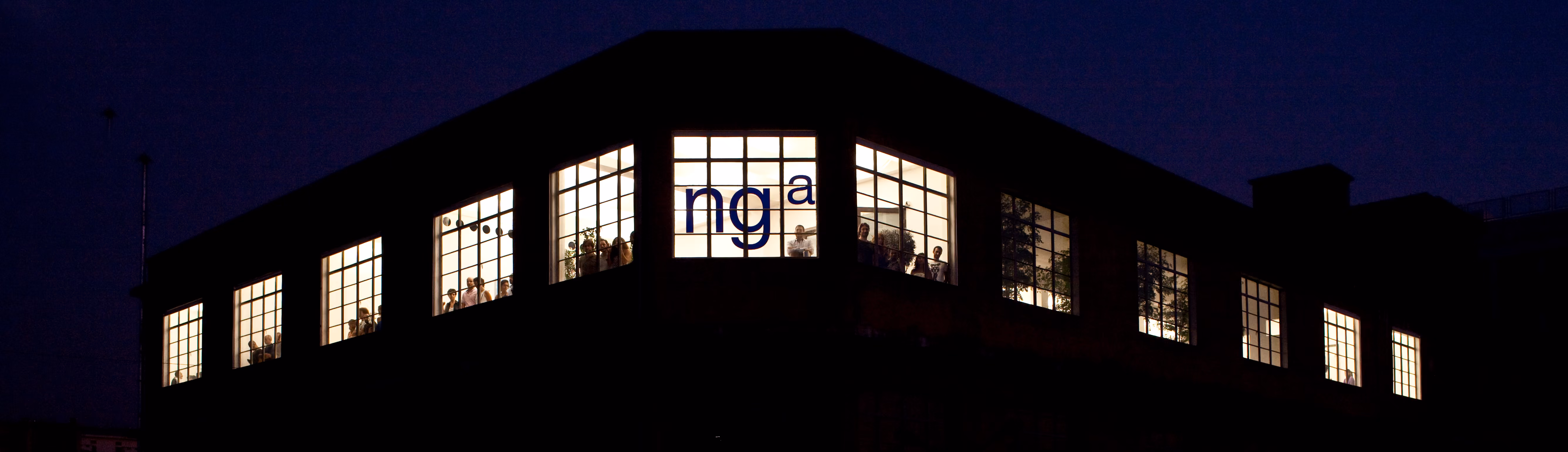 ngª Office in Beirut, night view of the illuminated building corner with the ngª logo lit in the windows and silhouettes of people inside