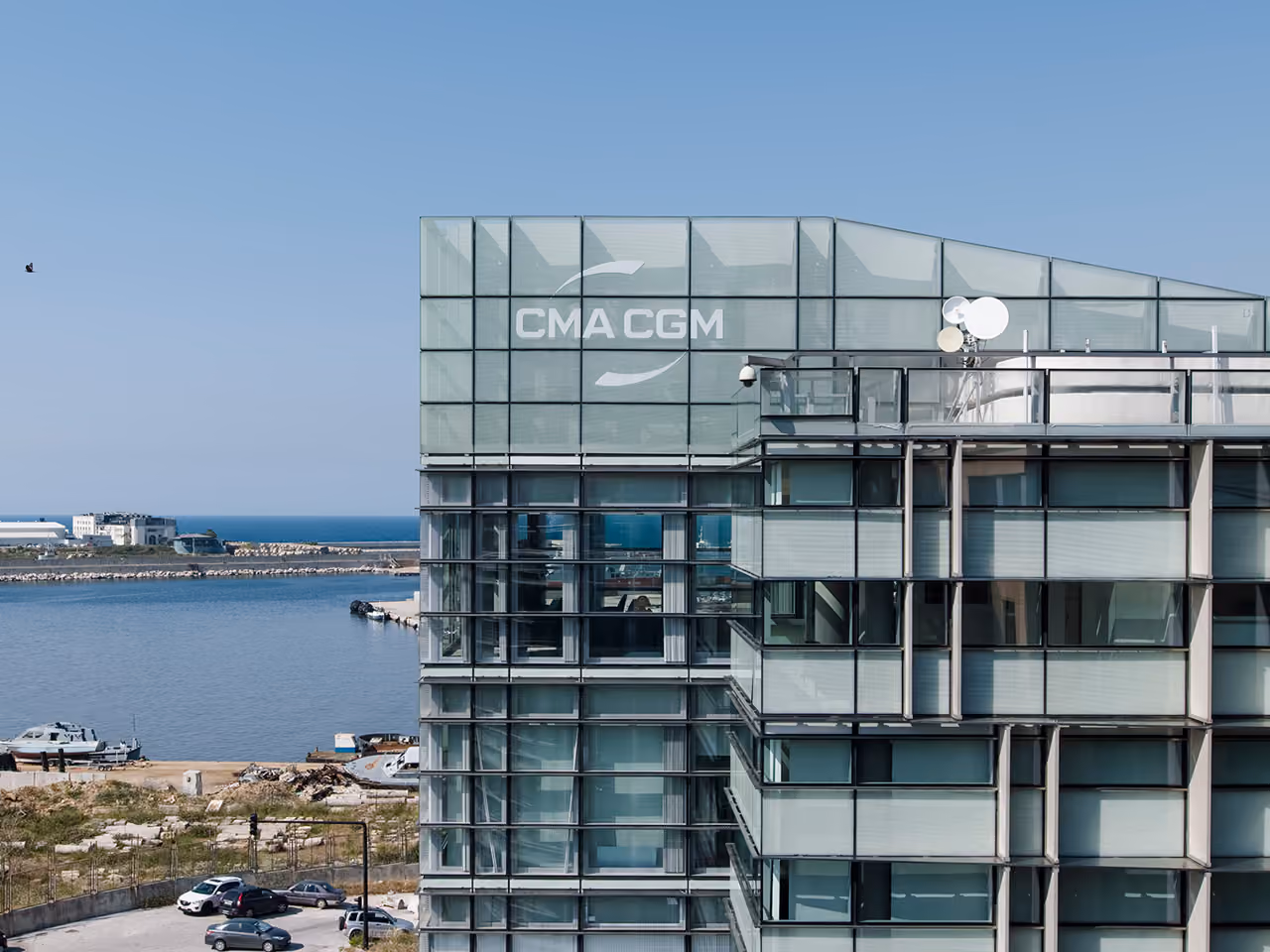 Angled glass corner of the CMA-CGM Headquarters in Beirut, displaying the company logo, overlooking the port and coastline below