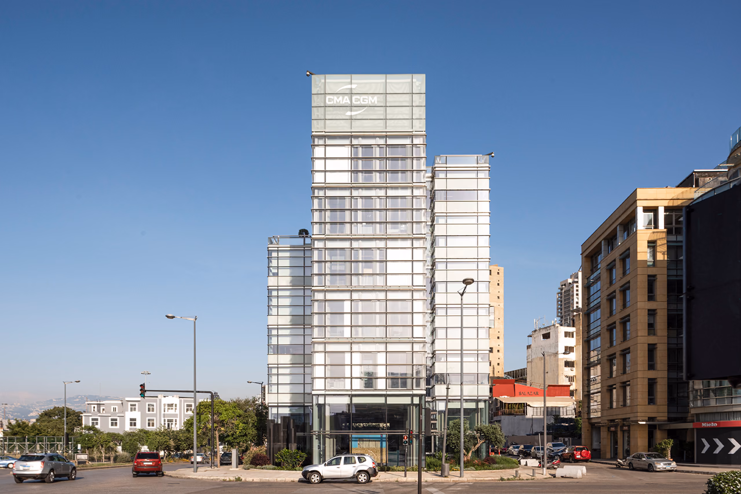 CMA-CGM Headquarters Refurbishment in Beirut, a glass-clad tower with layered volumes rising above street level traffic and neighbouring buildings under a clear sky