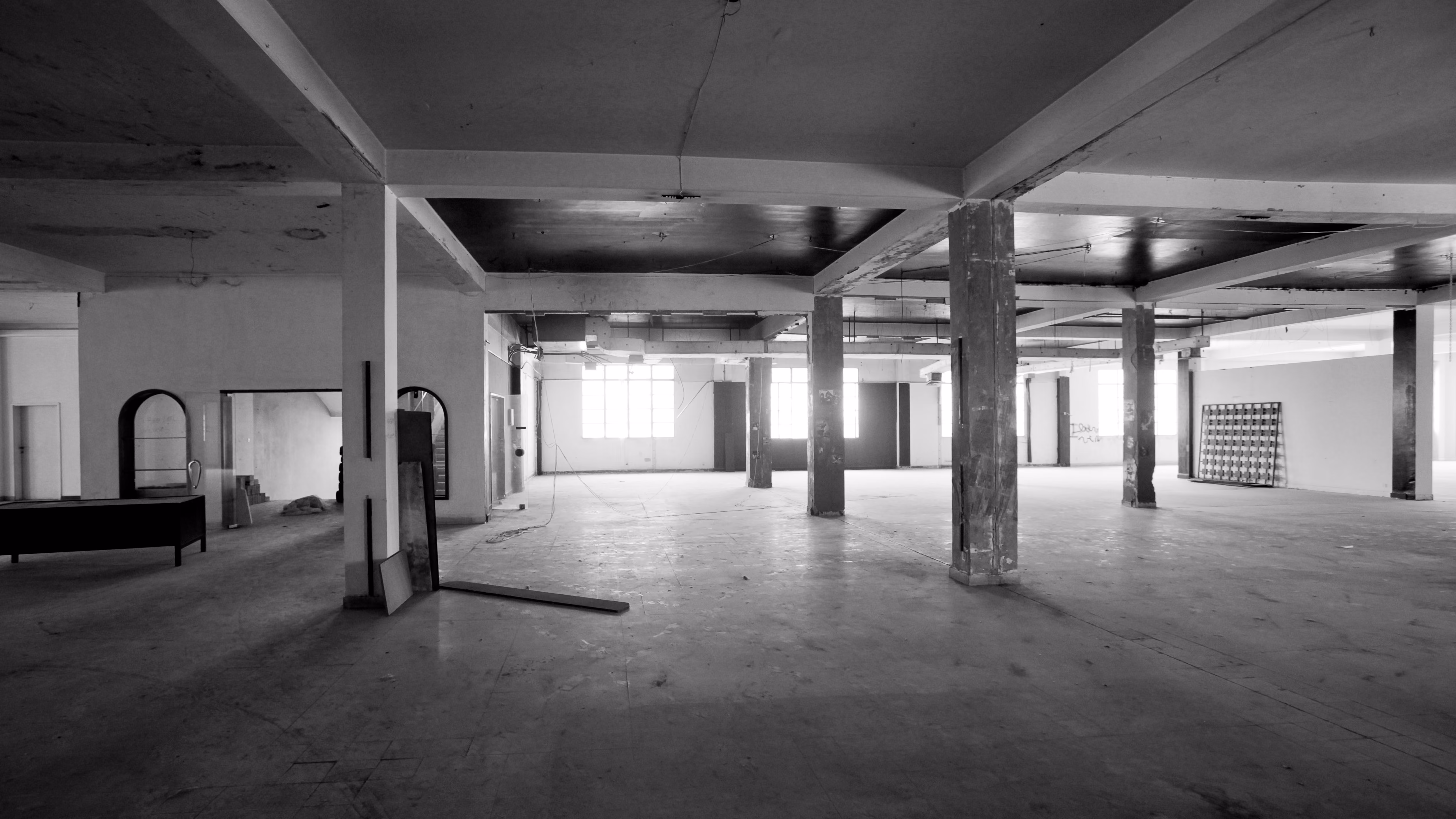 Black and white image of the raw industrial shell before renovation of ngª Office in Beirut, bare concrete columns and open floor plate lit by rows of windows