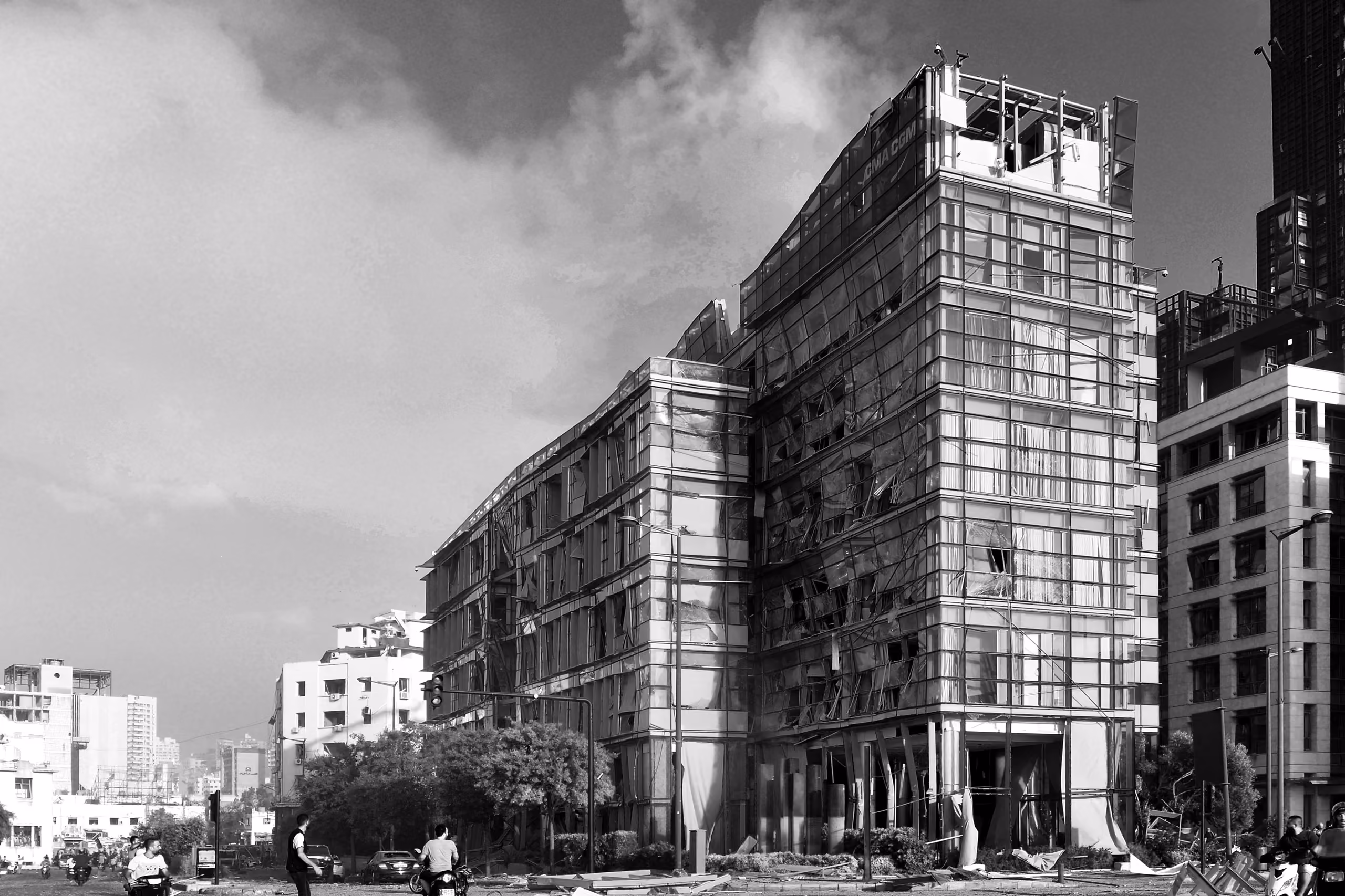 Black and white photograph of the CMA-CGM Headquarters in Beirut with shattered glazing and torn facade panels after the 2020 port explosion, amid the city skyline