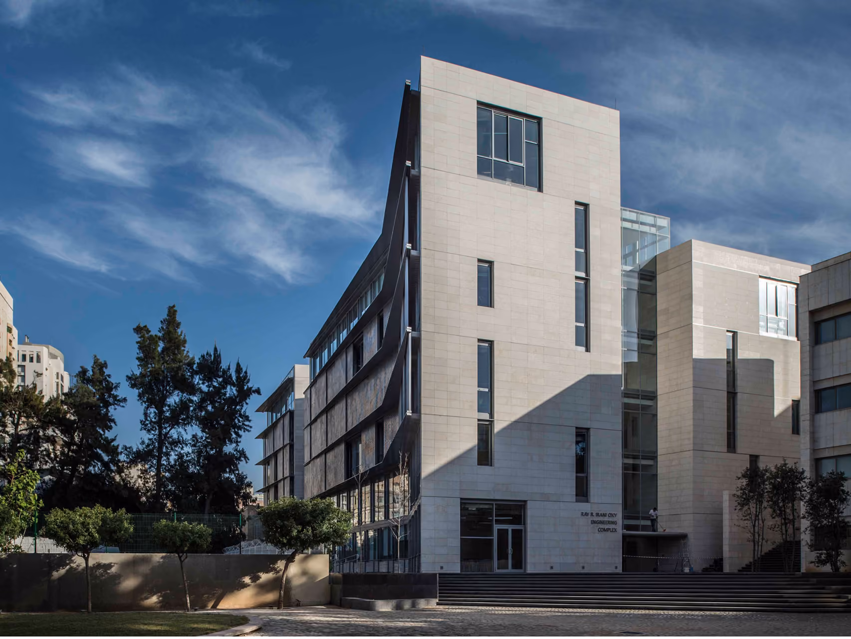 Angled stone facade of the AUB IOEC Engineering Labs in Beirut, with staggered window bands and a folded metal screen beside mature trees