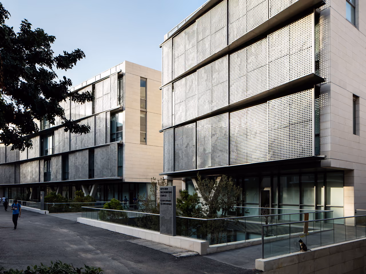 Perforated metal sunshades wrap the upper floors of the AUB IOEC Engineering Labs in Beirut, with a glazed ground level opening onto a landscaped courtyard