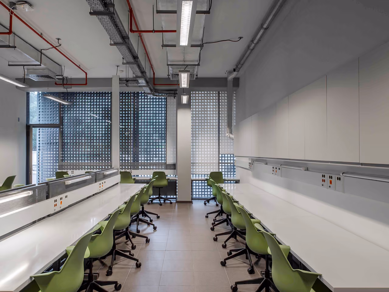 Engineering lab interior at AUB IOEC in Beirut with long white benches, green task chairs, exposed ceiling services and perforated screen windows