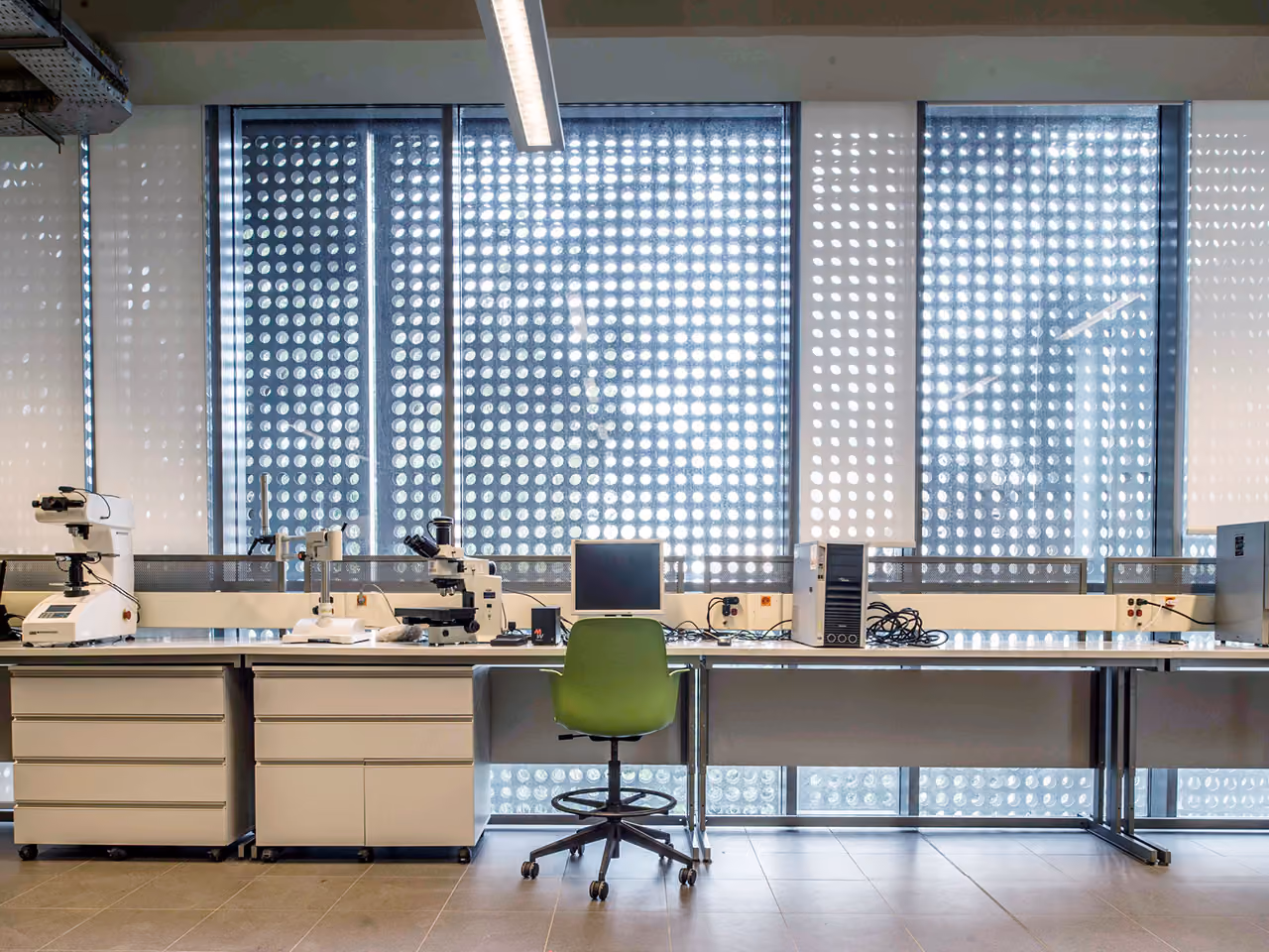 Laboratory workstation with microscopes and monitor in AUB IOEC Engineering Labs in Beirut, green chair before a perforated metal facade filtering daylight