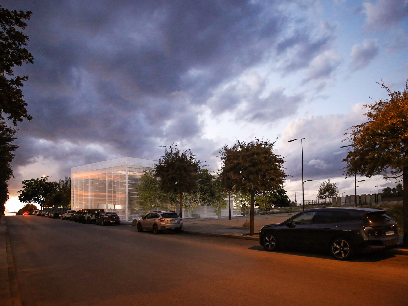 Art Hub in Beirut at dusk, a glowing glass-walled cube volume seen across a tree-lined street, parked cars in the foreground under a cloudy evening sky