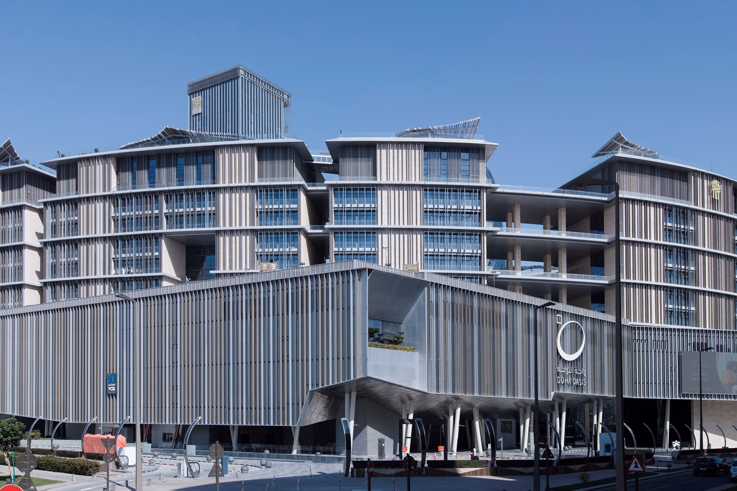 Doha Oasis in Doha, angled facade with vertical timber-effect louvers and tiered terraces, entrance canopy marked by a circular logo at street level