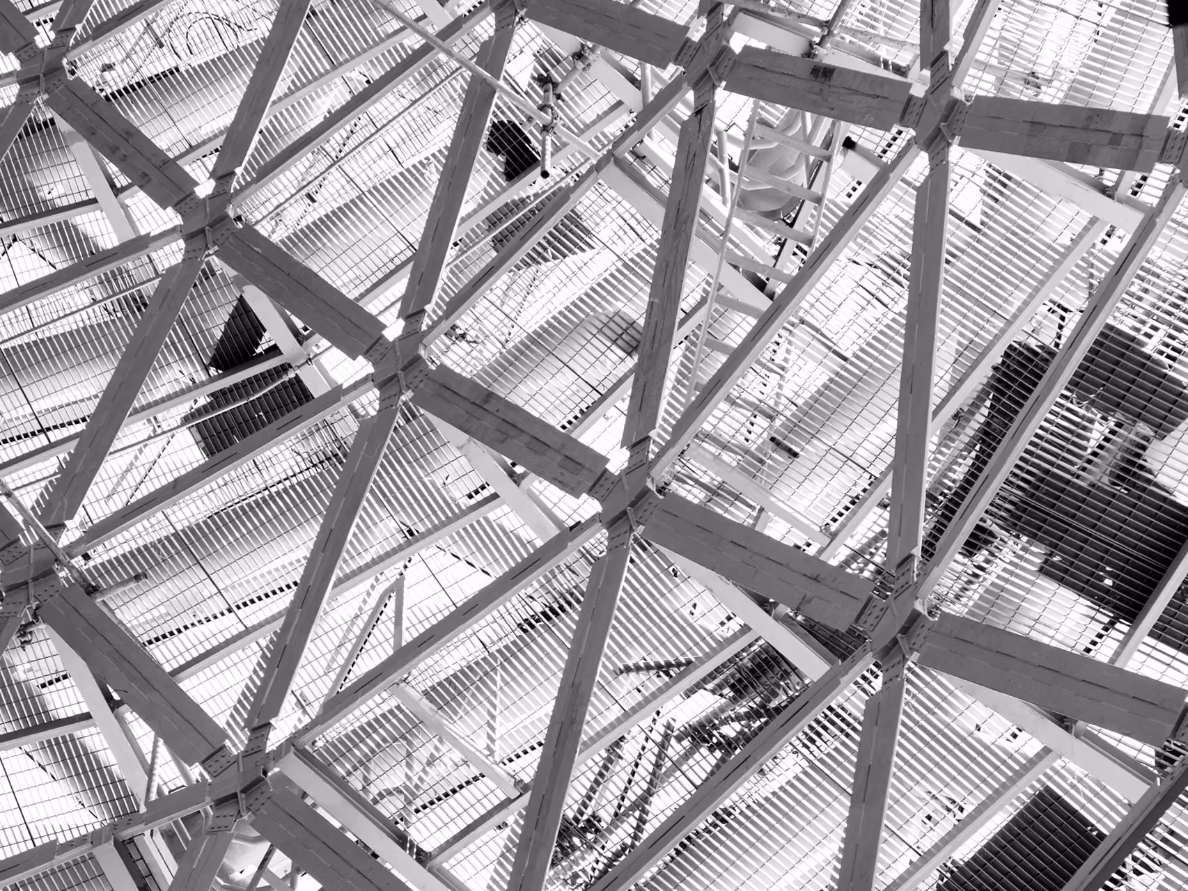 Black and white view looking up through a triangulated steel roof structure at Doha Oasis in Doha, layered trusses and mesh grating filtering light into the space below