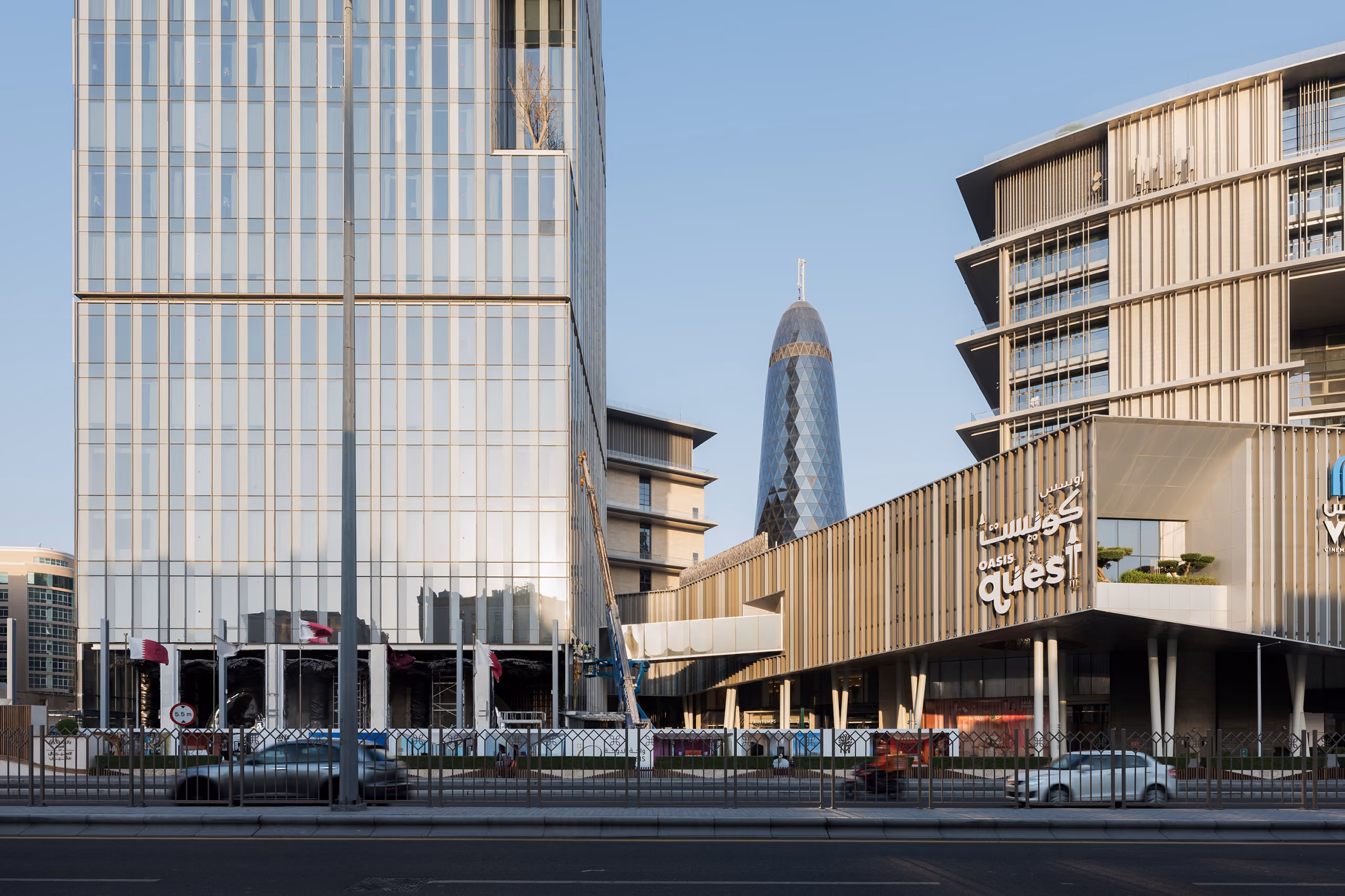 Street view of Doha Oasis in Doha, a glass office tower and louvred retail podium with the tapered Aspire Tower visible between the buildings