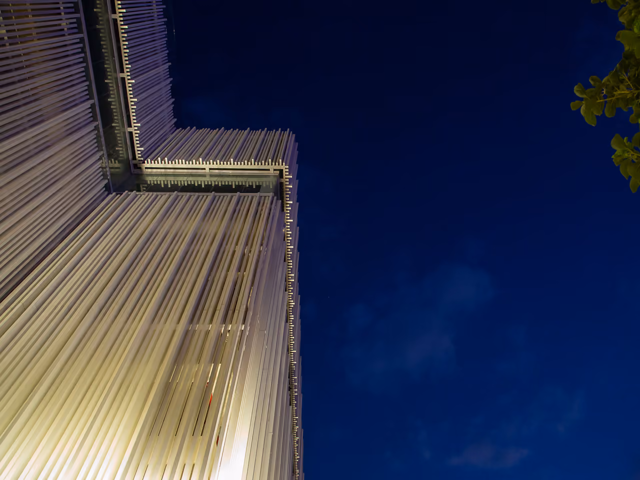 Upward night view of Dalfa Seafront in Beirut, vertical fin louvres wrapping the tower's corner illuminated against a dark blue sky