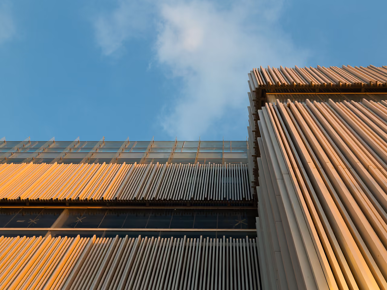 Upward view of Dalfa Seafront in Beirut, vertical sunshade fins catching golden light against a blue sky with glazed setbacks below