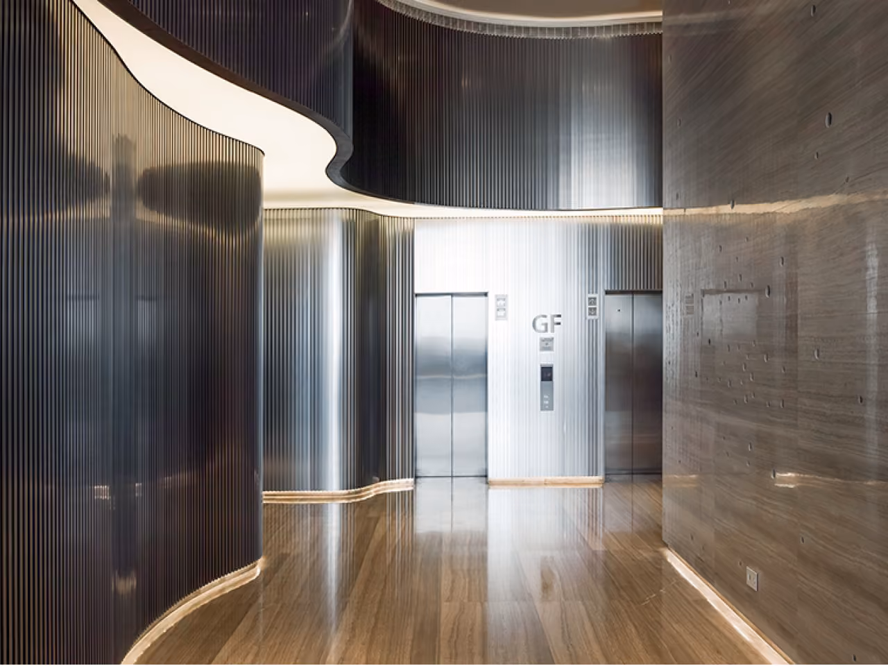 Ground floor elevator lobby in Dalfa Seafront, Beirut, with fluted metal wall panels, a curved illuminated ceiling and polished wood flooring