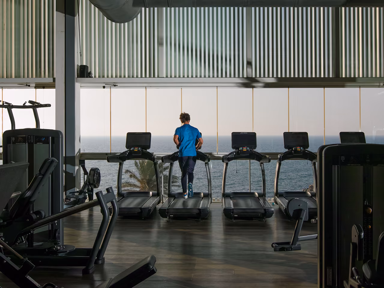 Gym at Dalfa Seafront in Beirut, a runner on a treadmill facing floor-to-ceiling windows overlooking the Mediterranean Sea
