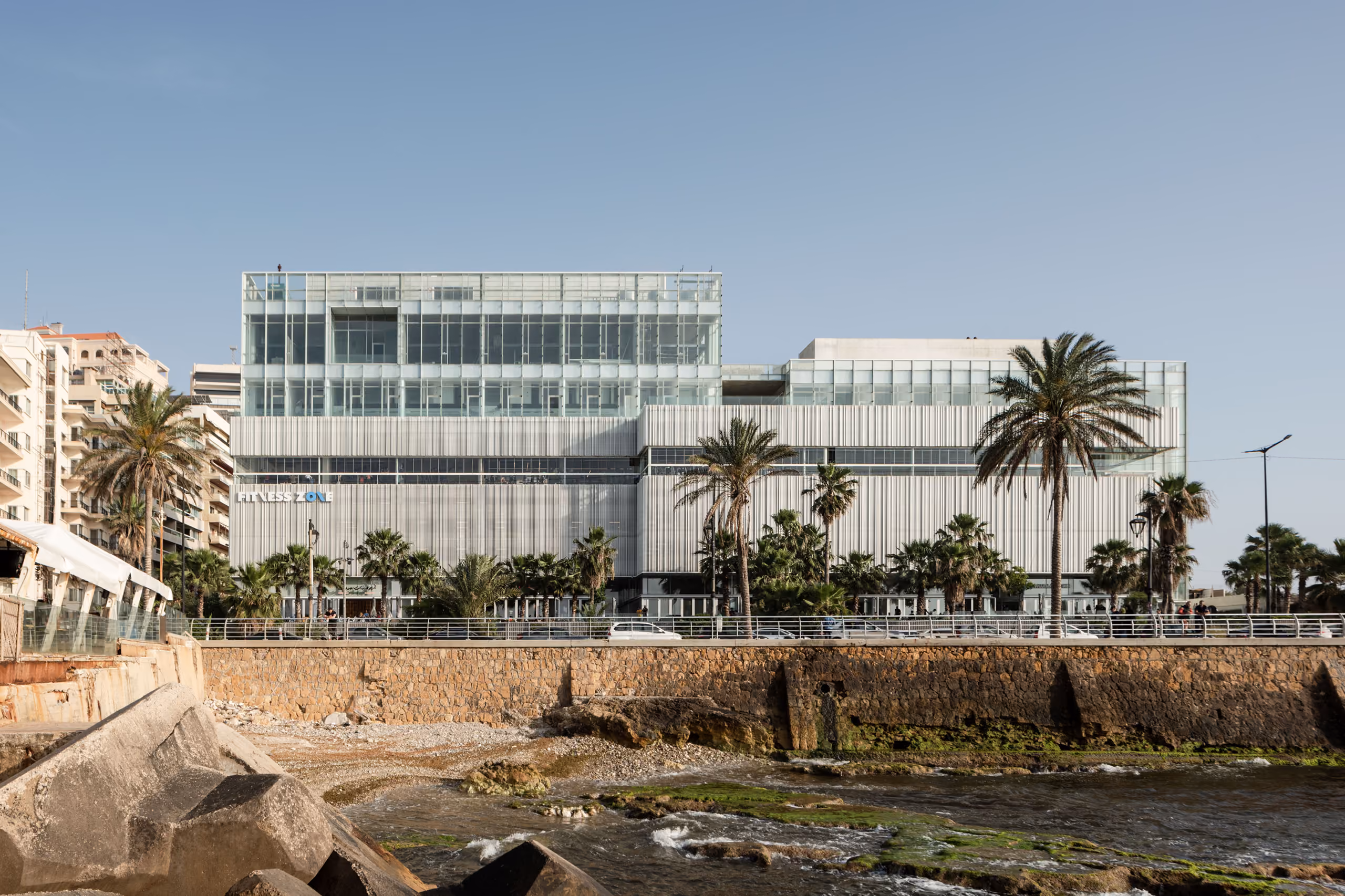 Dalfa Seafront in Beirut, ribbed metal-clad volumes with a glazed rooftop level, seen from the rocky shoreline along the Corniche