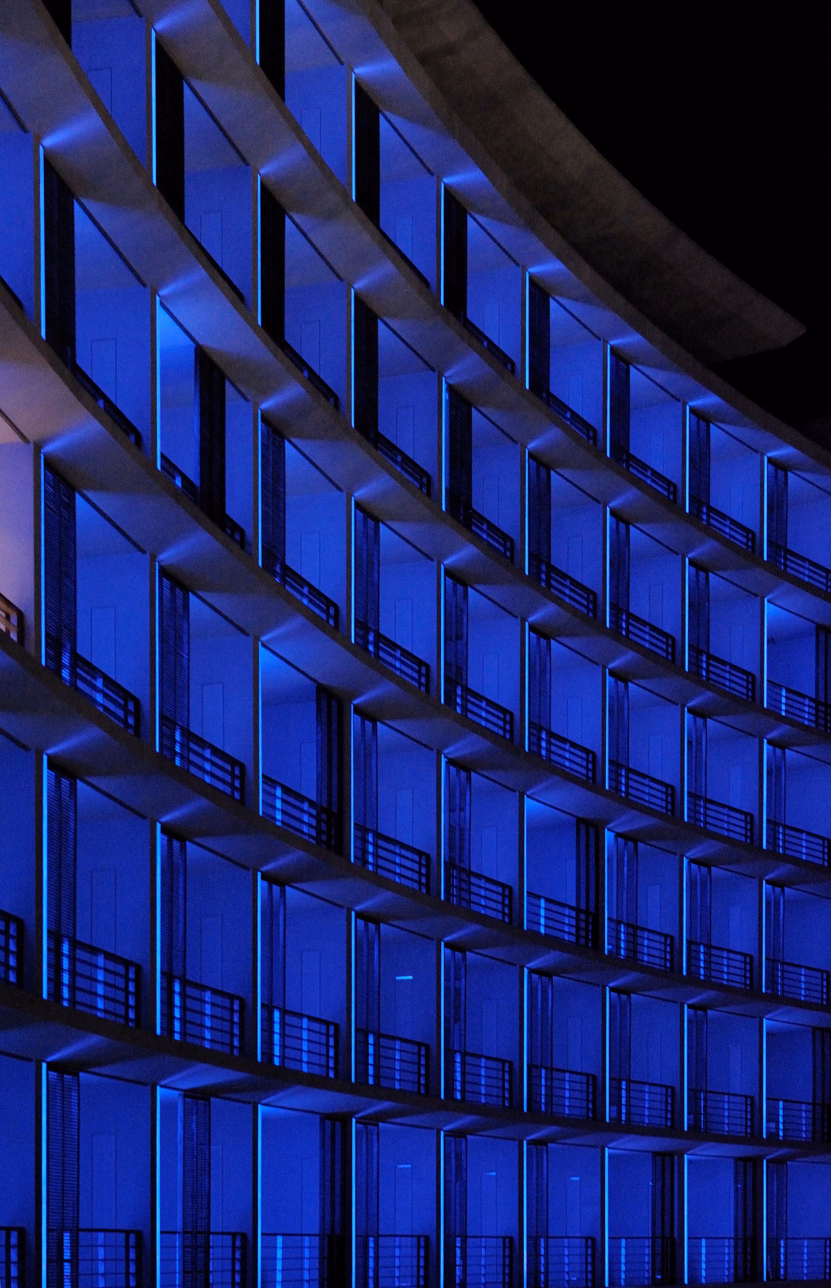Curved facade of the Kempinski Hotel in Aqaba at night, tiered balconies glowing deep blue in a repeating diagonal grid pattern
