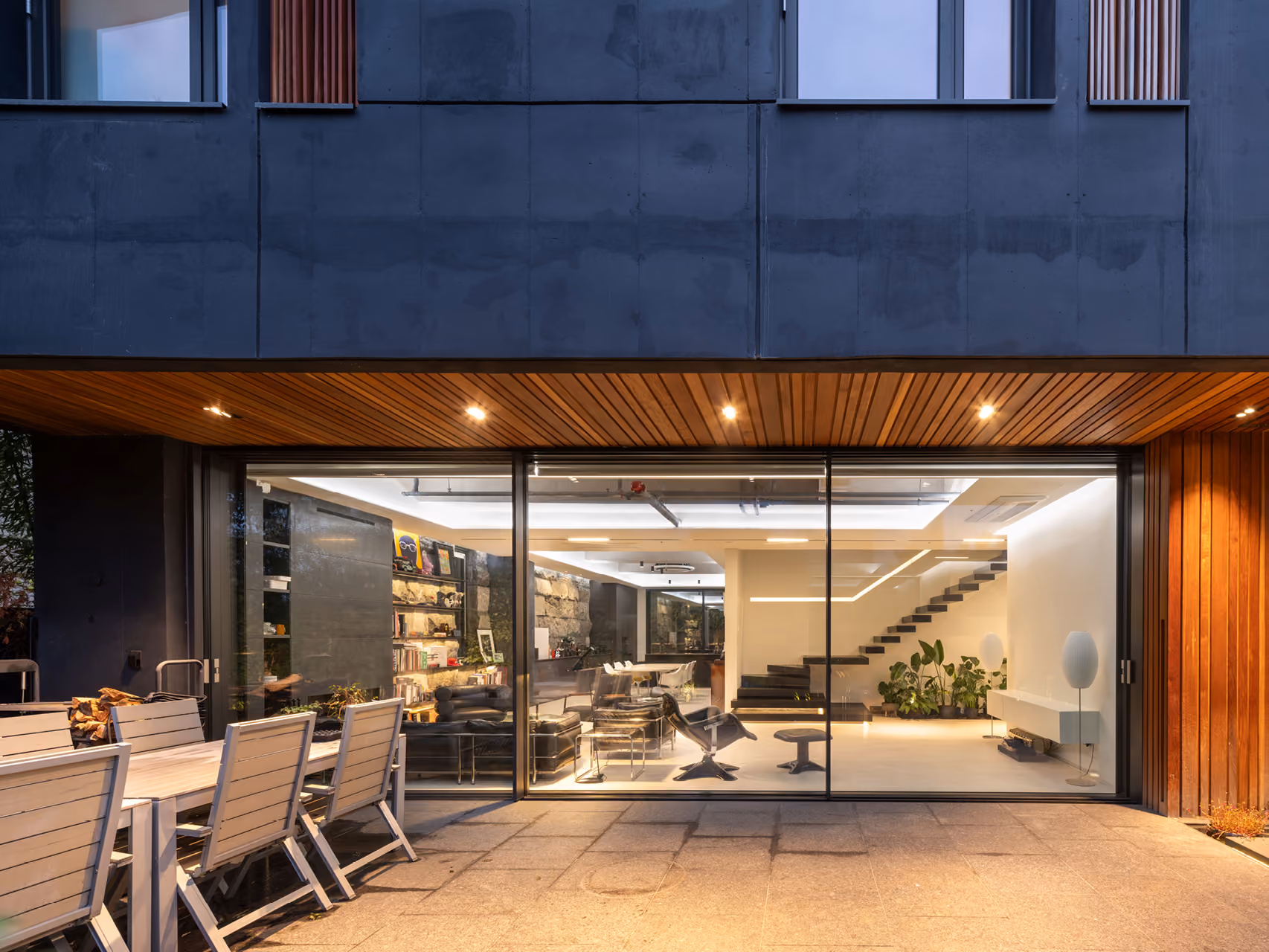 Ground floor lounge of Pyrite in Seoul opens onto a stone terrace, glass walls revealing bookshelves, black leather seating and a floating black staircase