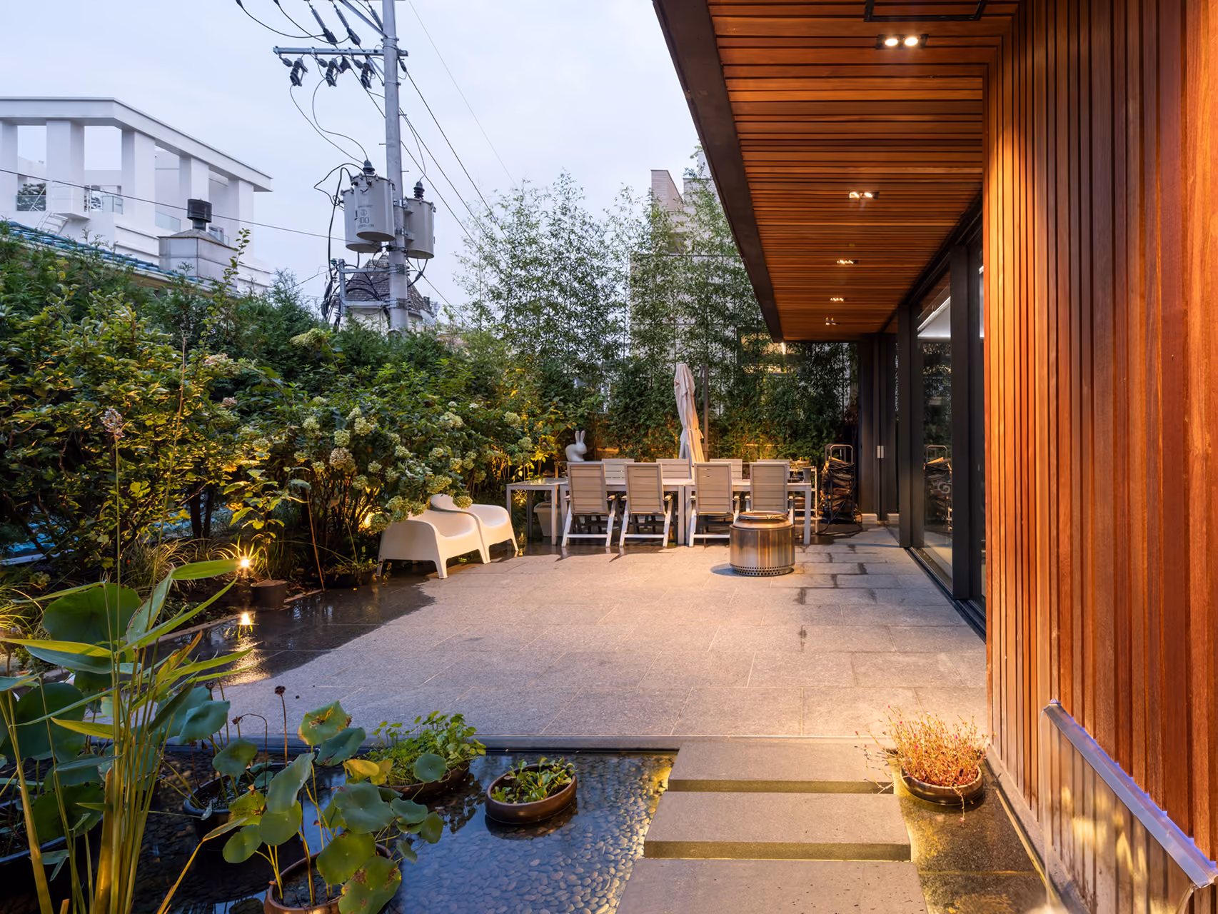 Terrace of Pyrite in Seoul, timber-clad overhang above a stone patio with outdoor seating and a small lily pond bordered by lush greenery