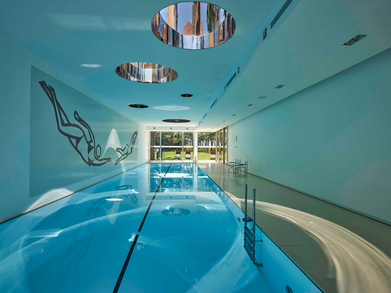 Indoor lap pool at The House with Two Lives in Bois de Boulogne, circular skylights above, diver mural on the wall and glazed end opening to a garden