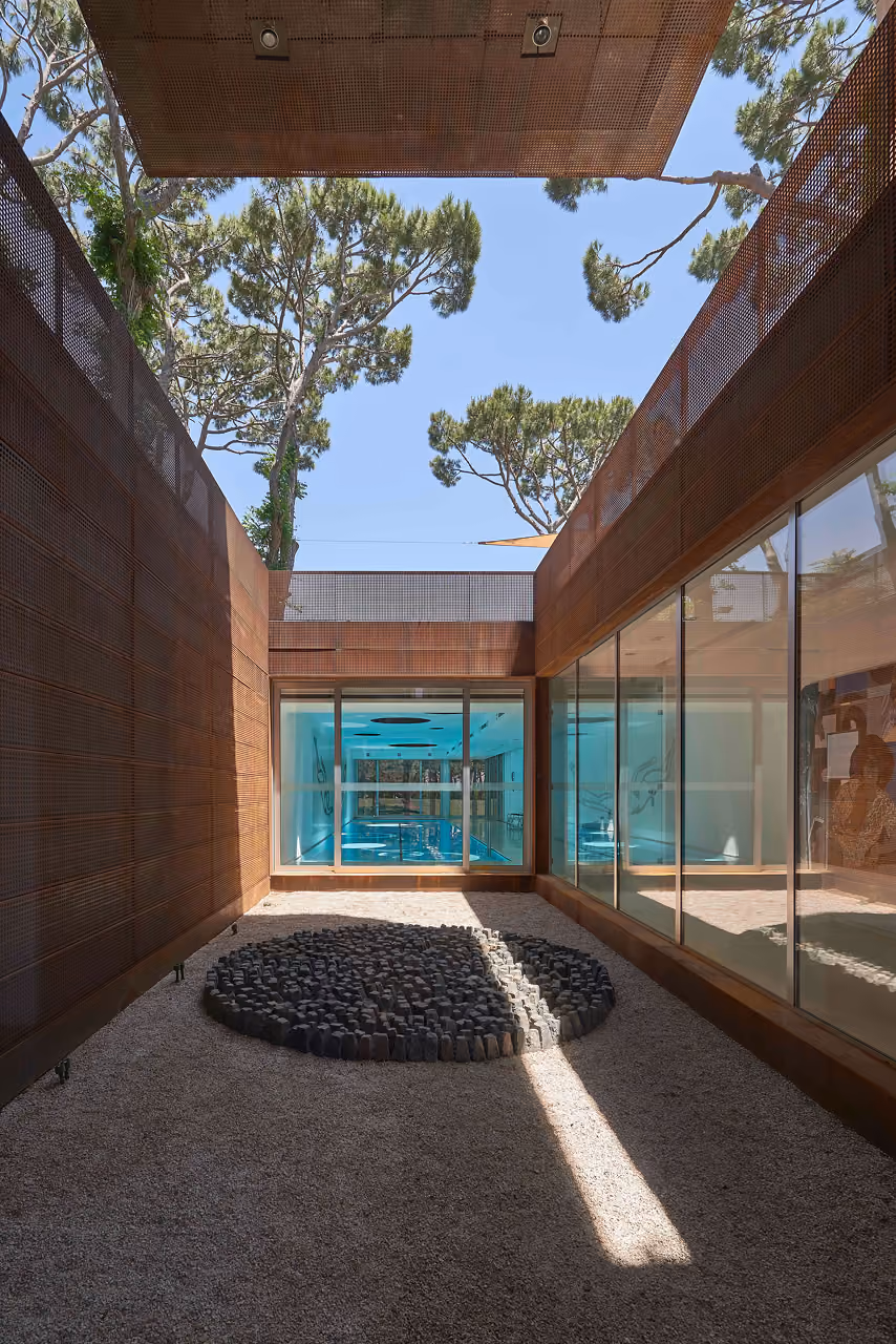 Corten steel-clad courtyard at The House with Two Lives in Bois de Boulogne, gravel garden with circular stone arrangement leading to a glazed indoor pool