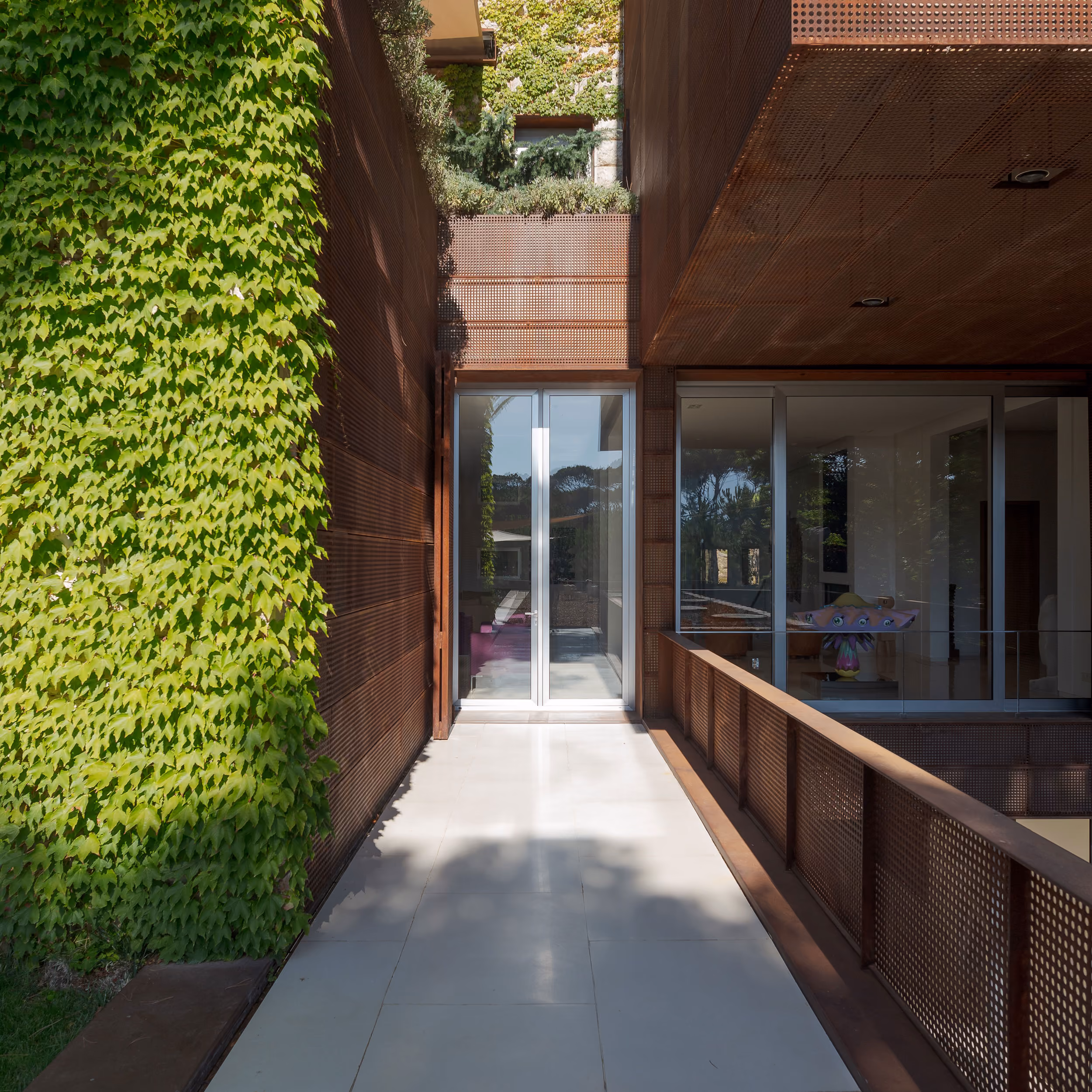 Corten steel-clad walkway at The House with Two Lives in Bois de Boulogne, ivy-covered wall beside perforated metal railing leading to glazed entrance