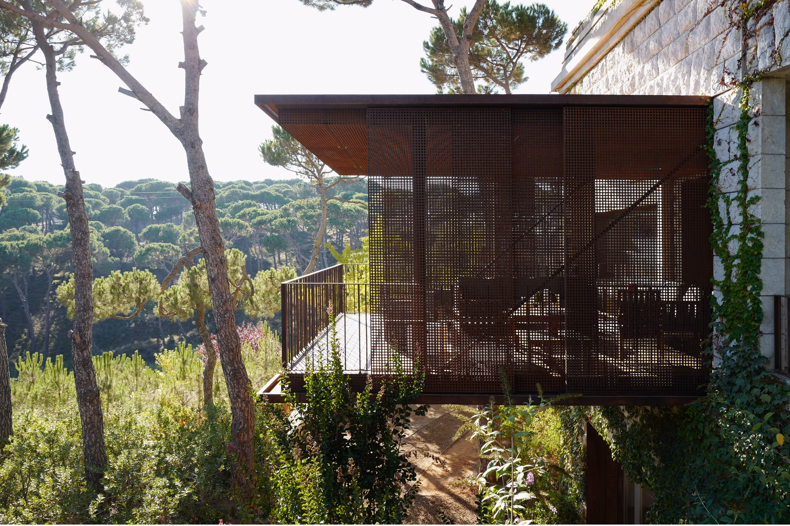 Perforated Corten steel volume cantilevering from the stone facade of The House with Two Lives in Bois de Boulogne, overlooking a pine forest