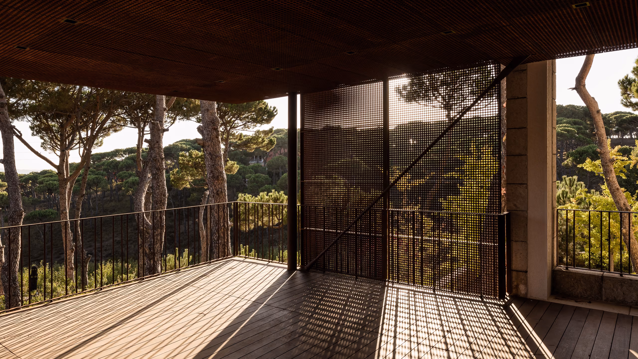Perforated Corten steel screen casts dappled shadows on a wooden terrace overlooking pine trees at The House with Two Lives in Bois de Boulogne