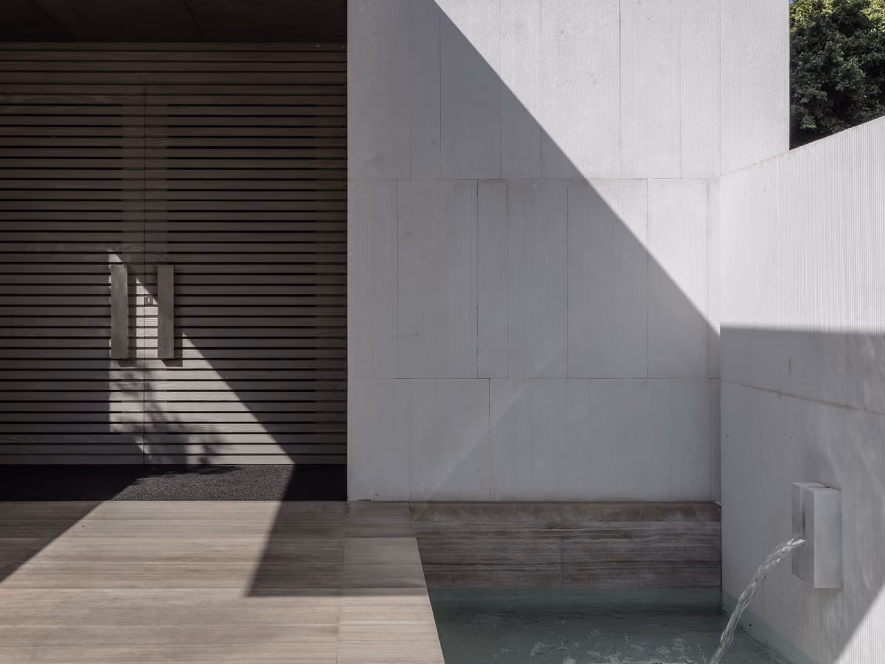 Entrance detail at AZ House in Adma, timber slatted door beside a white stone wall with a small wall fountain trickling into a pool