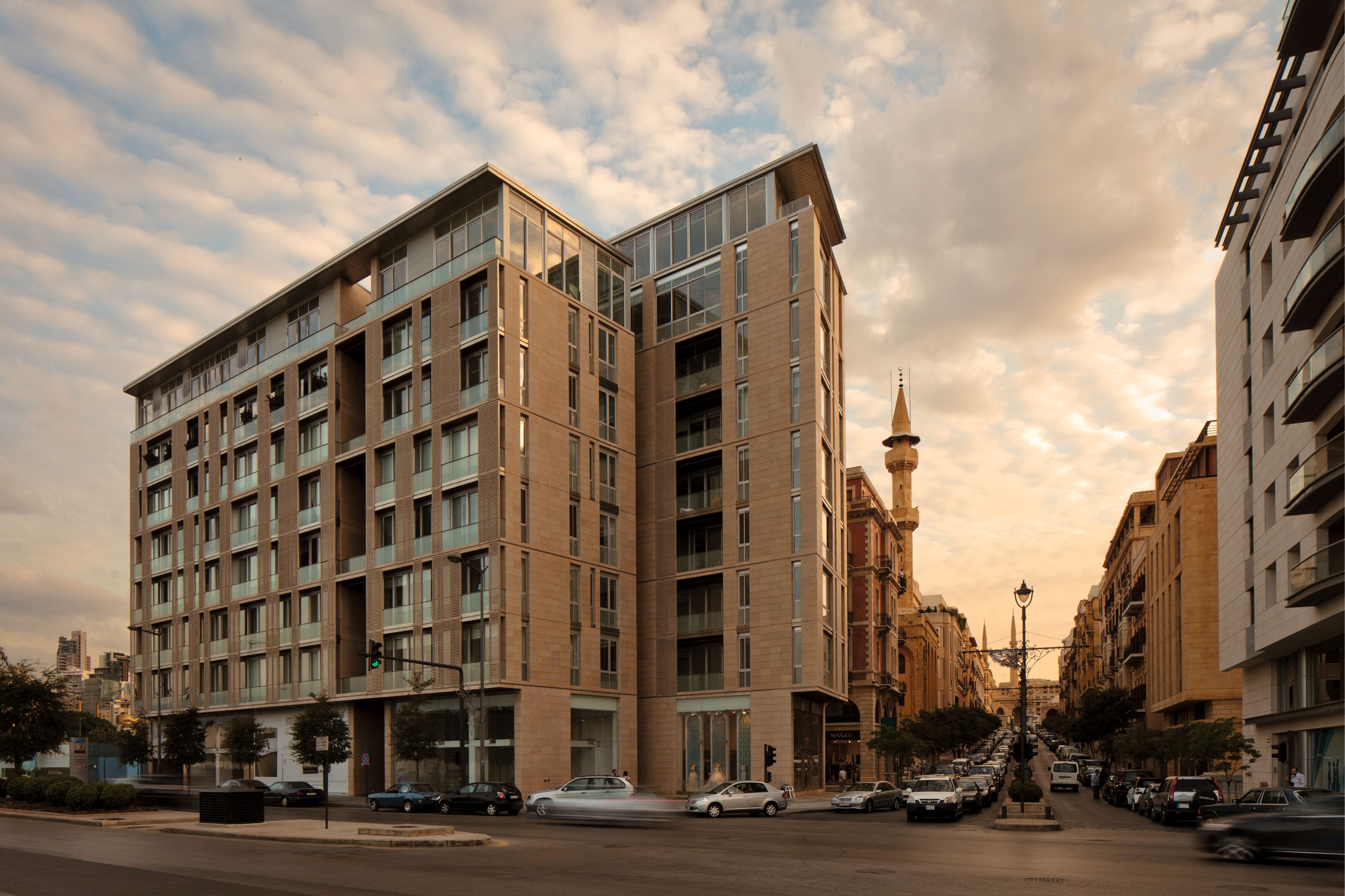 Foch 94, a stone-clad residential building by Nabil Gholam Architects, split into two towers along a tree-lined street near a mosque minaret in Beirut Central District, Lebanon