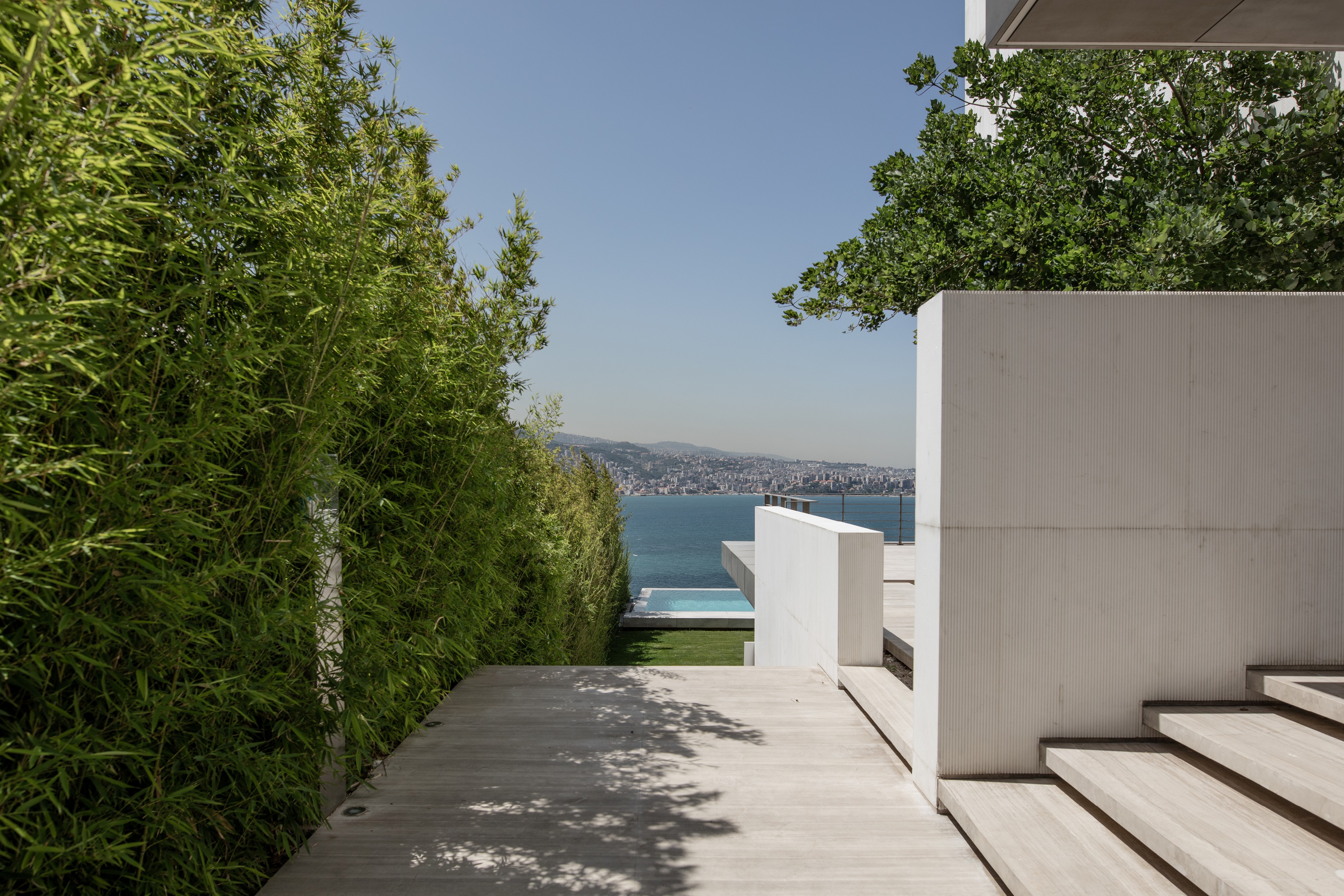 AZ House by Nabil Gholam Architects in Adma, Lebanon, a white concrete residence with a wooden terrace overlooking a pool and the Mediterranean coastline