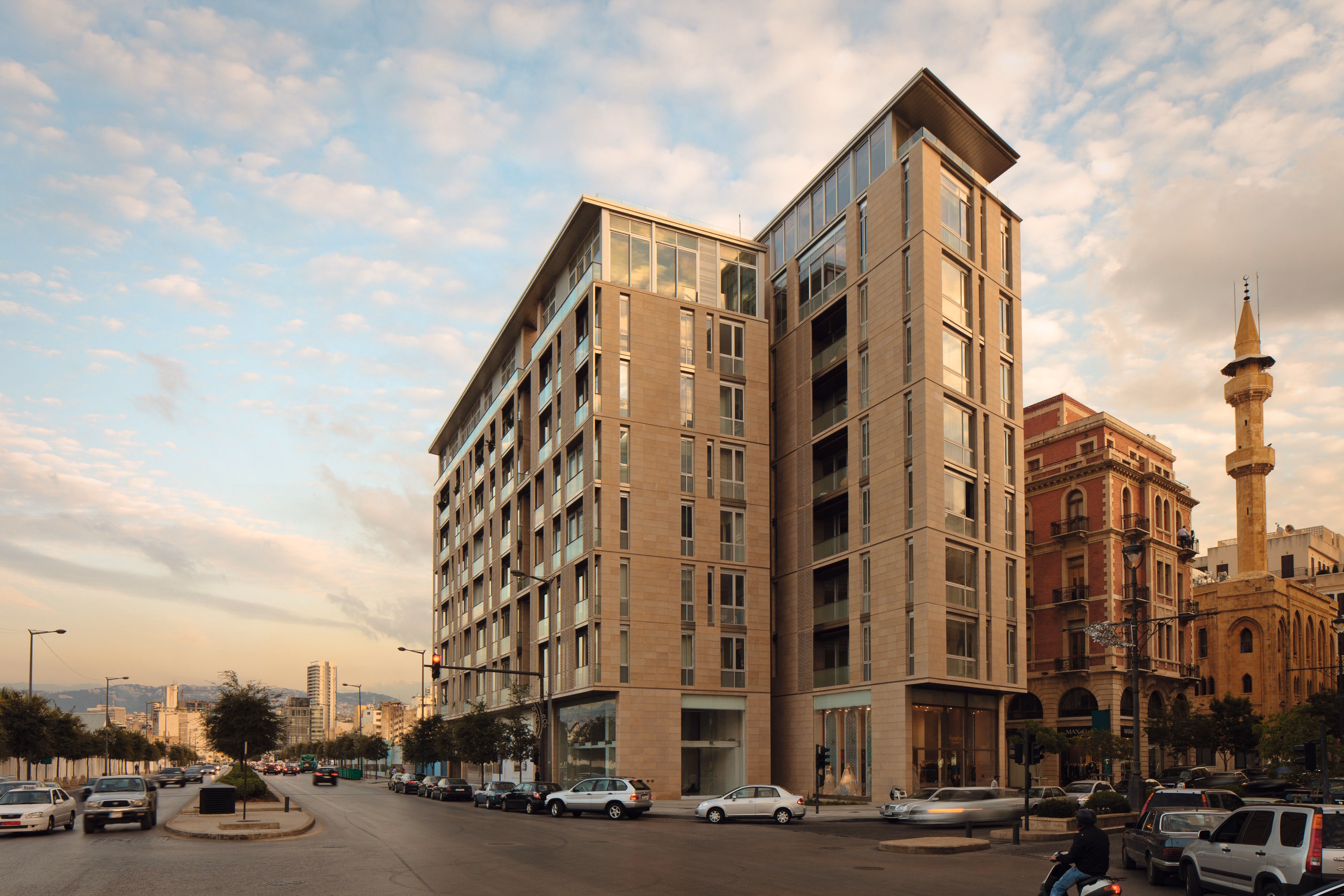Foch 94 in Beirut Central District, a stone-clad residential building split into two towers beside a historic mosque with minaret at dusk