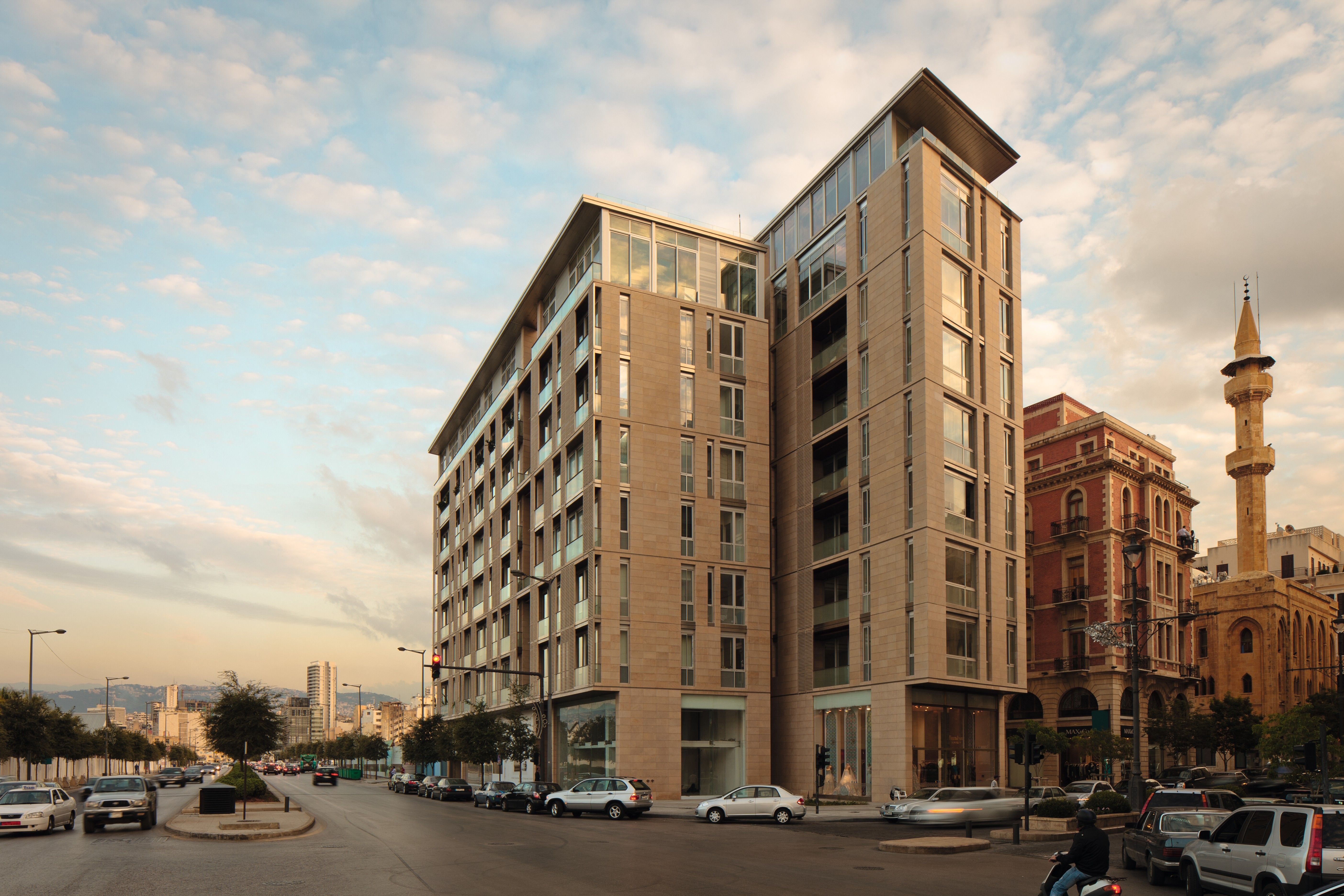 Foch 94 in Beirut Central District, a stone-clad residential building split into two towers beside a historic mosque with minaret at dusk
