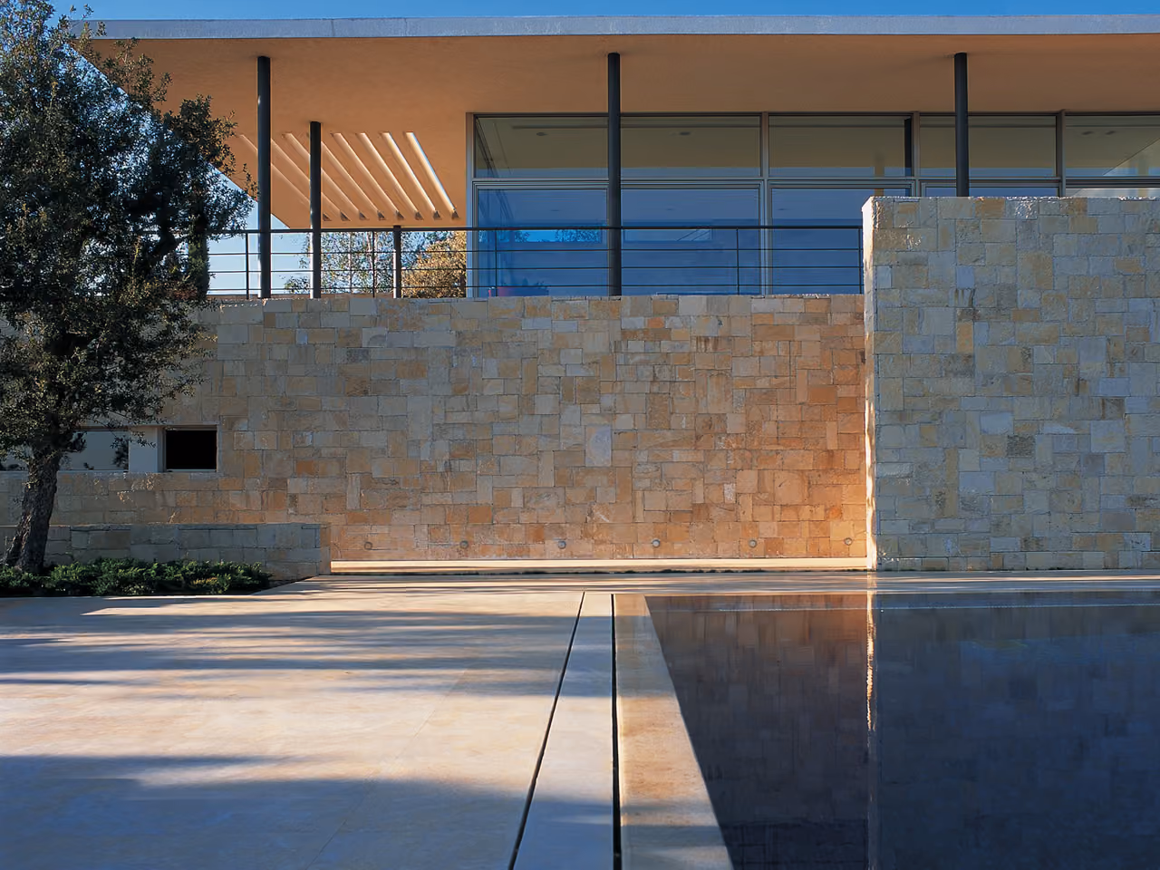 Stone-clad walls and a reflecting pool at F House in Dahr el Sawan, with a cantilevered canopy and glazed upper level framed by slender columns