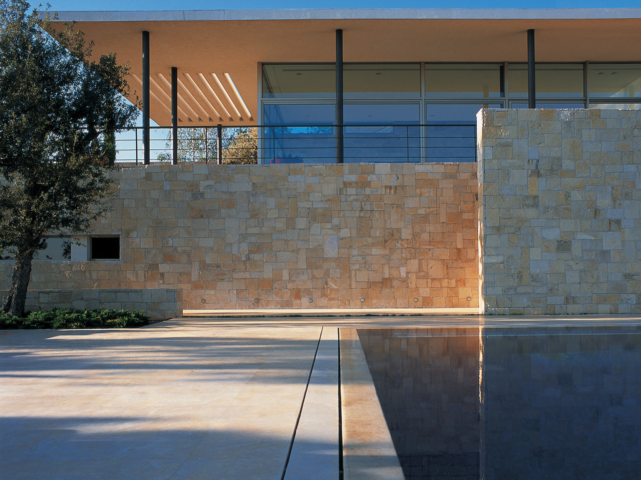 Stone-clad walls and a reflecting pool at F House in Dahr el Sawan, with a cantilevered canopy and glazed upper level framed by slender columns