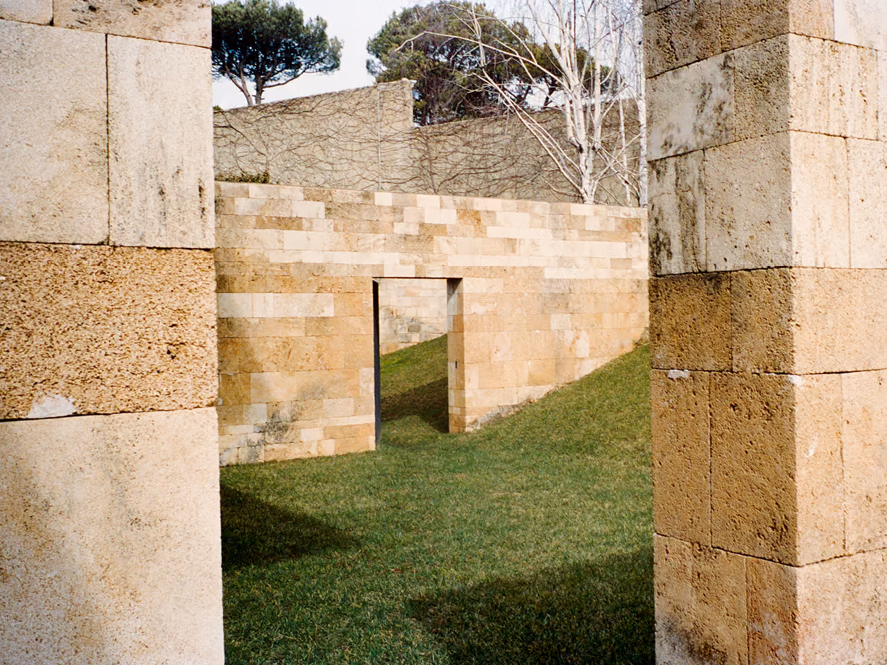 Sandstone garden walls with a narrow doorway cut into them, framed by two large stone piers, at F House in Dahr el Sawan, Lebanon