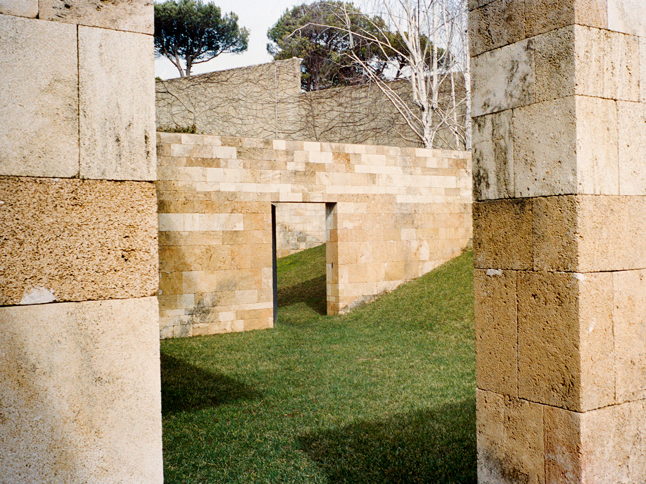 Sandstone garden walls with a narrow doorway cut into them, framed by two large stone piers, at F House in Dahr el Sawan, Lebanon