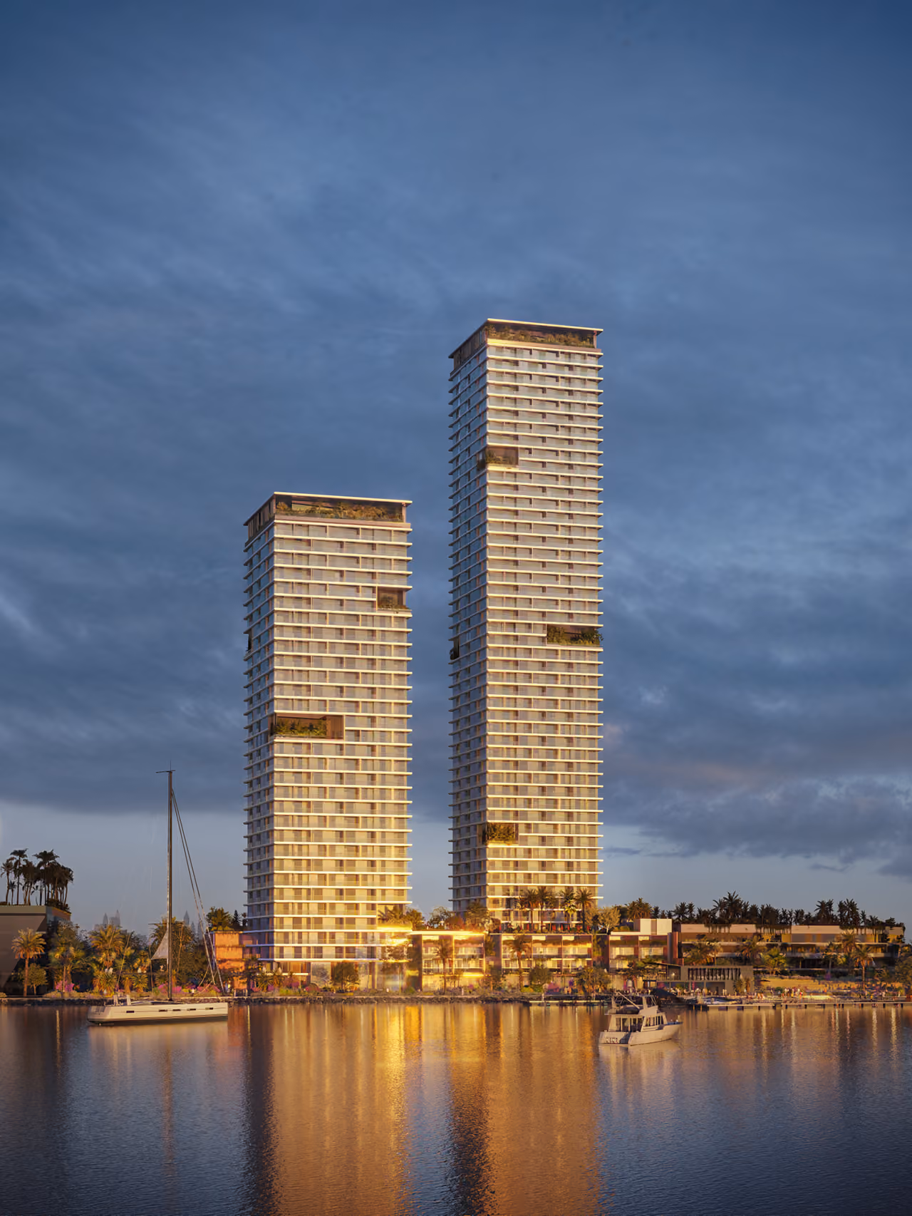 Orise's twin residential towers in Dubai lit at dusk, rising above a waterfront marina with yachts moored against a cloudy blue sky