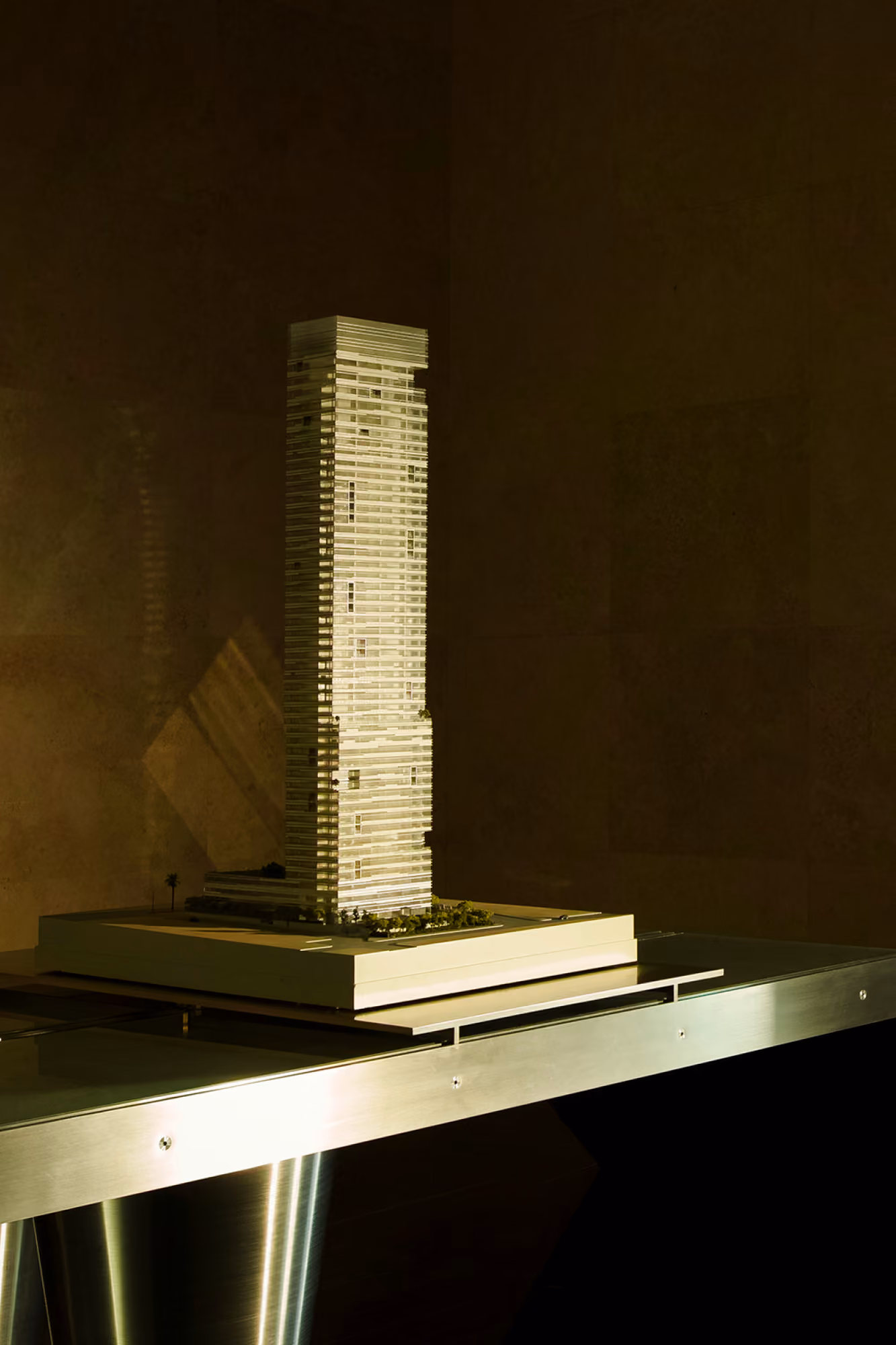Scale model of Golden Tower in Jeddah, an illuminated slender high-rise on a base with landscaping, displayed on a glass table in a dark room