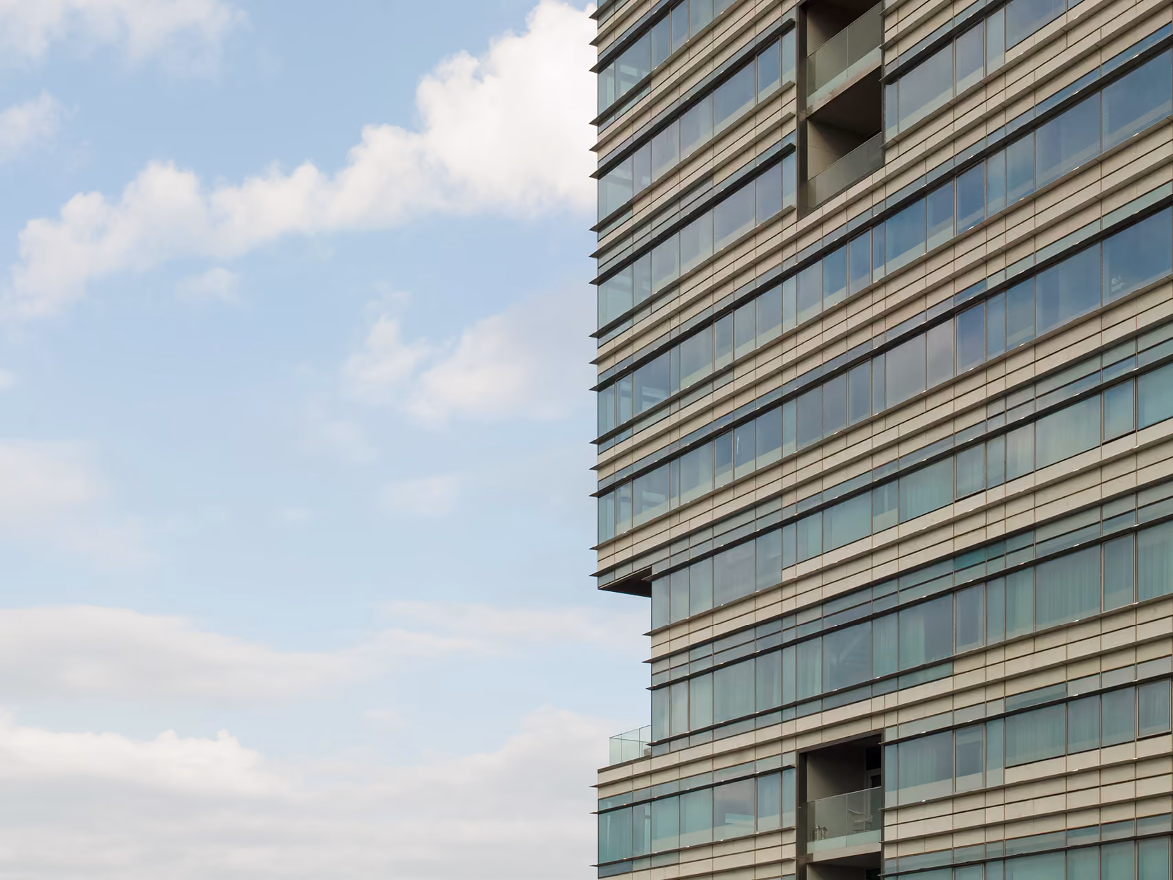 Facade detail of Golden Tower in Jeddah, stacked horizontal bands of glazing and stone-coloured spandrels with recessed corner balconies against a partly cloudy sky