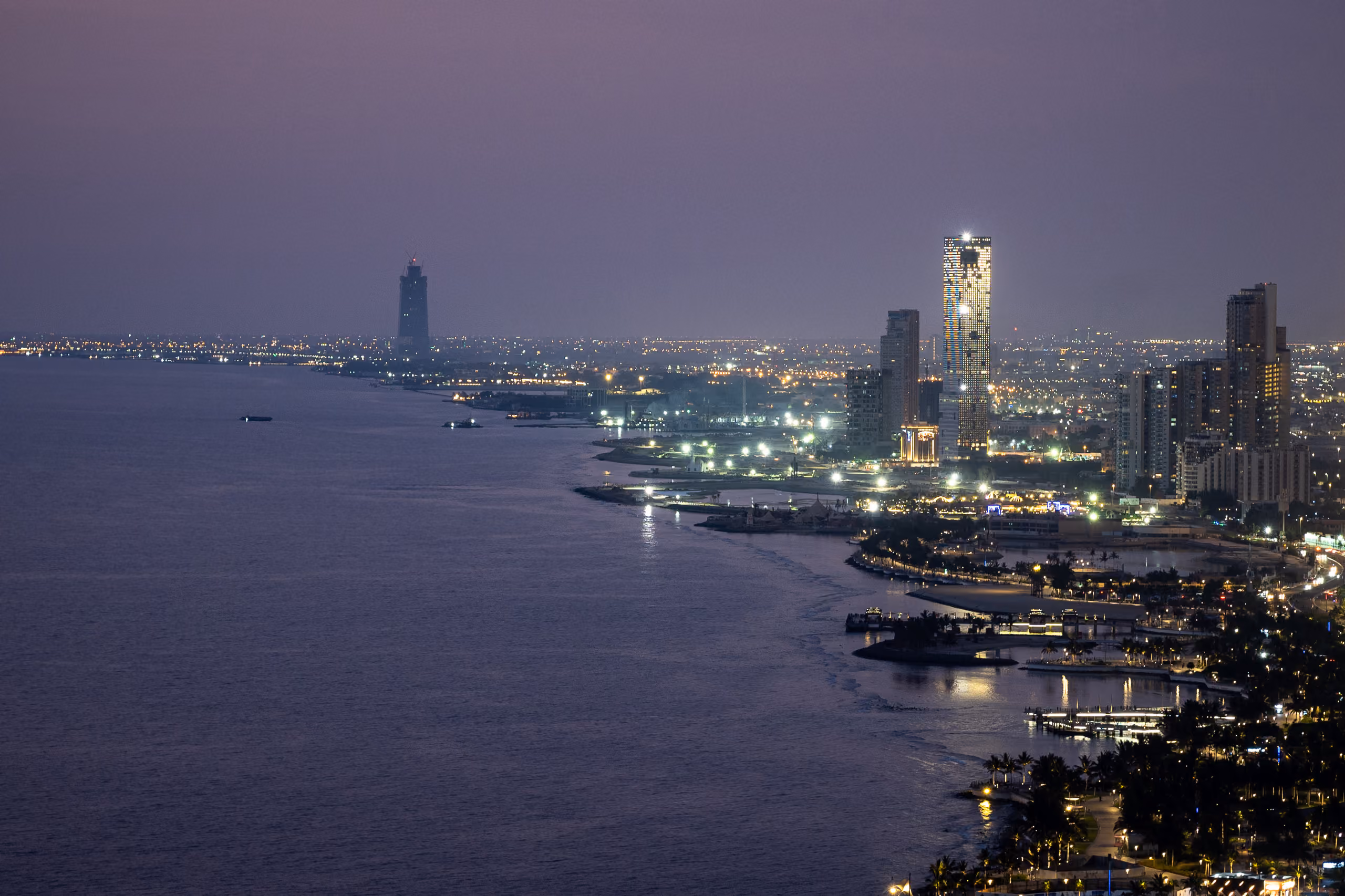 Golden Tower illuminated at dusk along Jeddah's seafront corniche, its faceted glass facade standing out among the city's coastal skyline